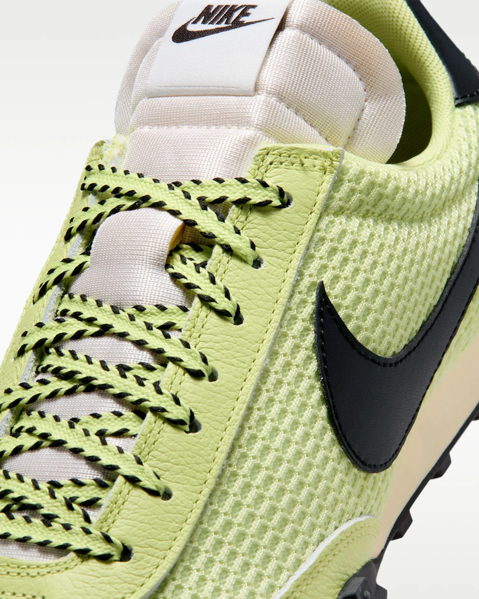 Close-up of a light green Nike sneaker with black-accented laces and a black Nike swoosh on mesh fabric.