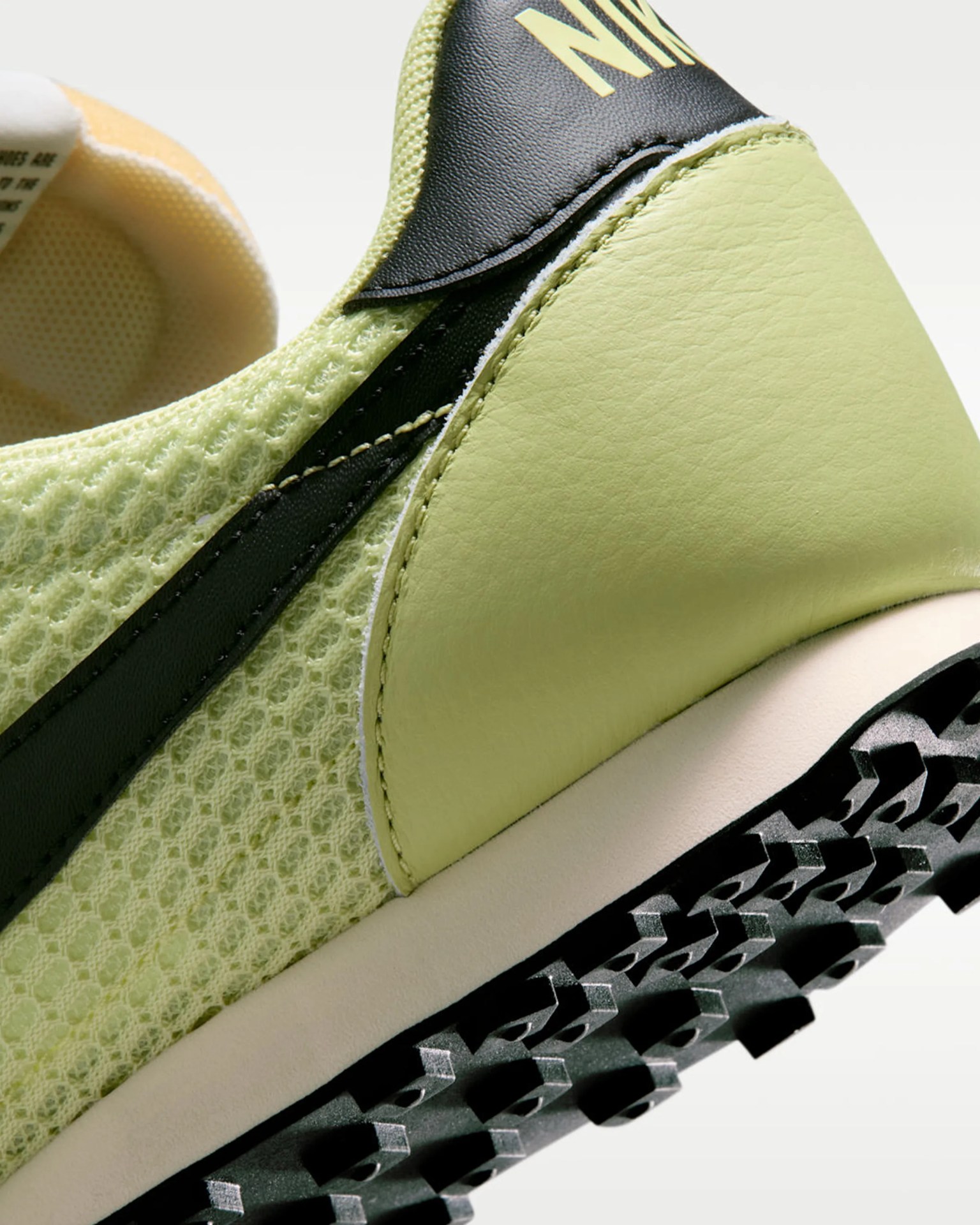 Close-up of a light green Nike sneaker with black swoosh, textured mesh upper, and rugged black sole.