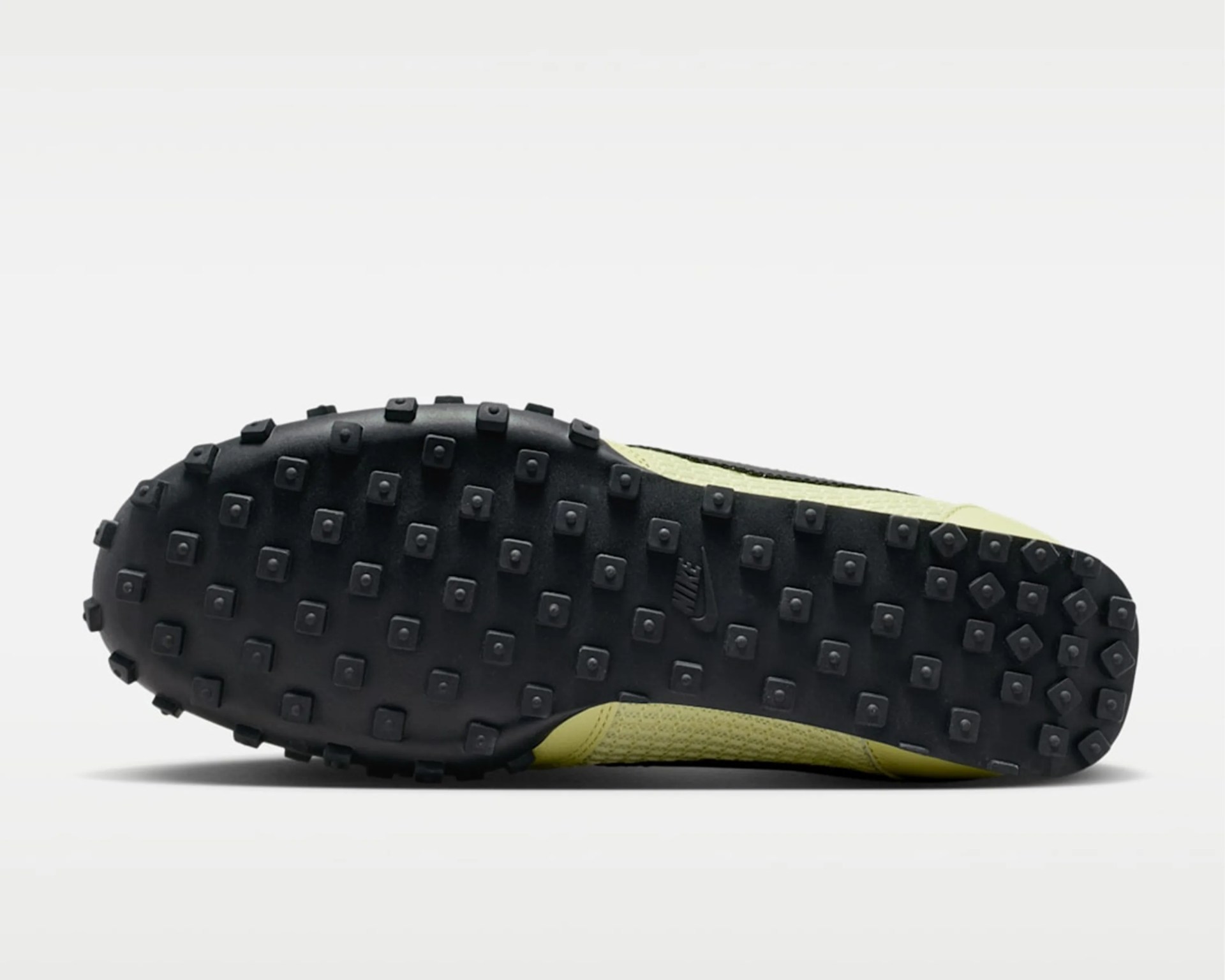 Black rubber sole with square studs and a small Nike logo on a yellow shoe.