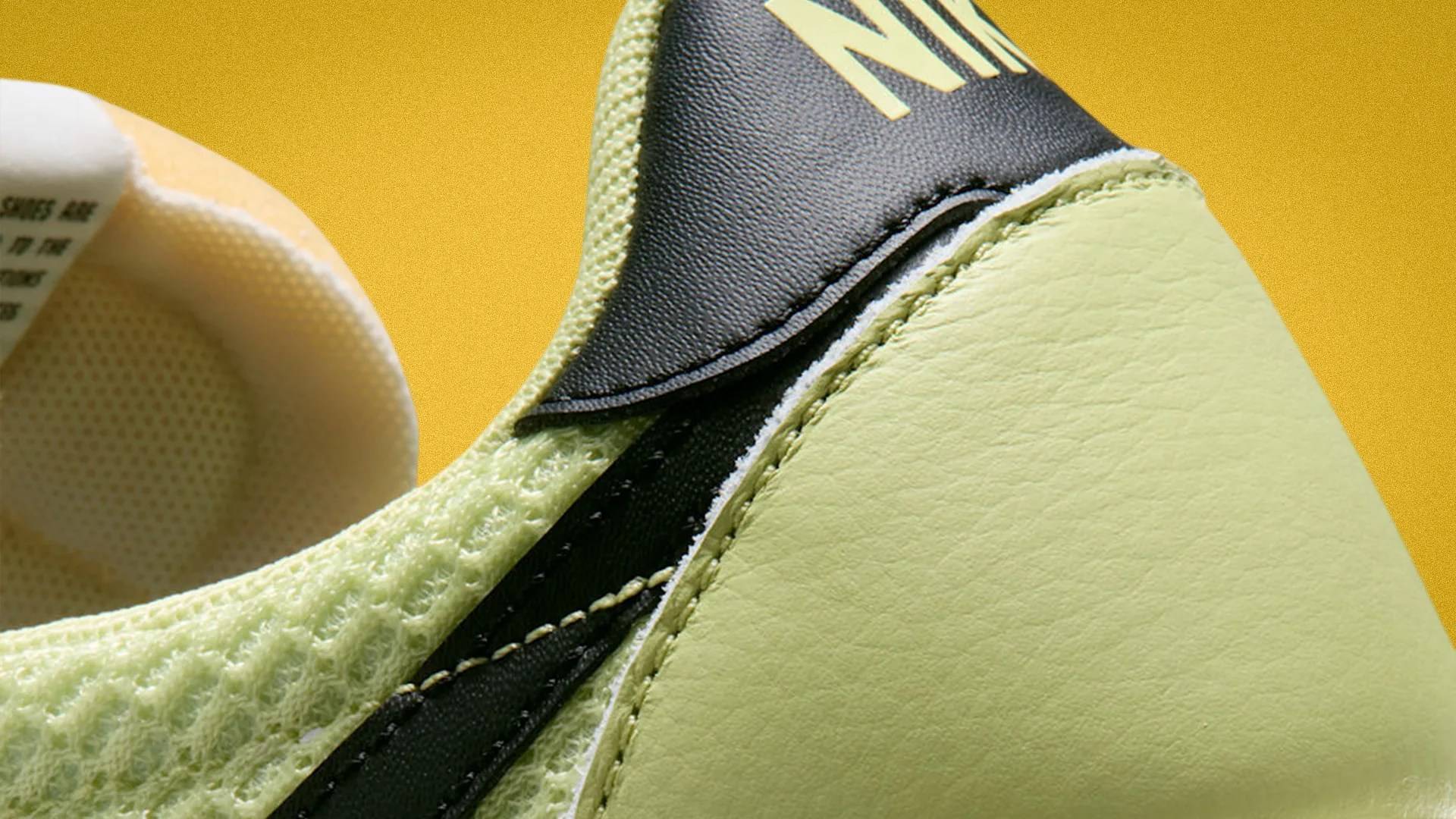 Close-up of a light green Nike sneaker with black and yellow accents on a yellow background.