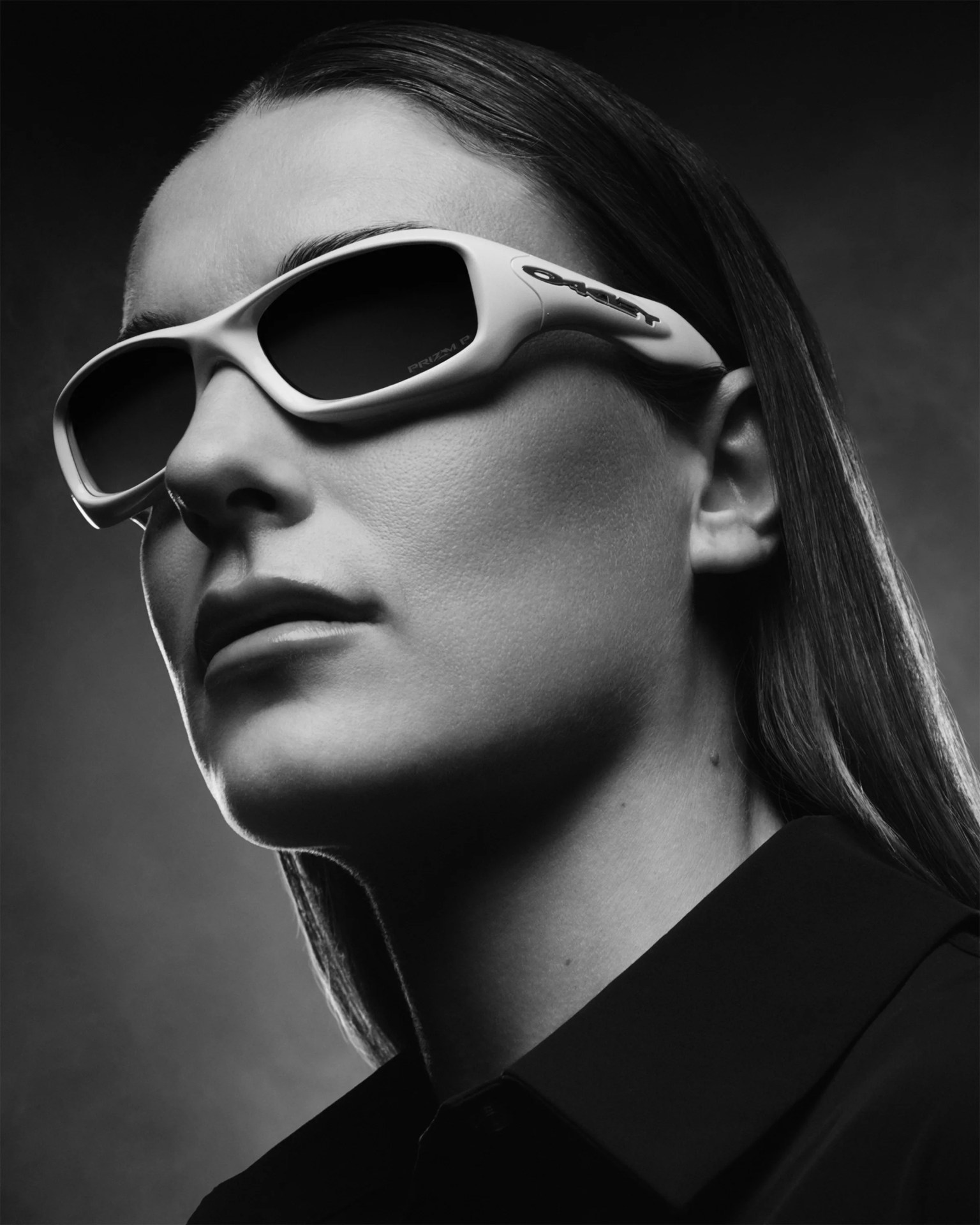 Close-up of a person wearing white Oakley sunglasses with dark lenses and a black collared shirt.