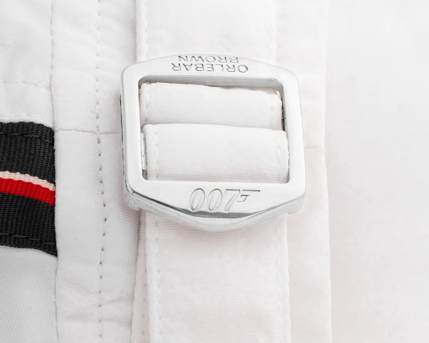 Silver metal buckle engraved with "007" and "Orlebar Brown" on a white fabric strap.