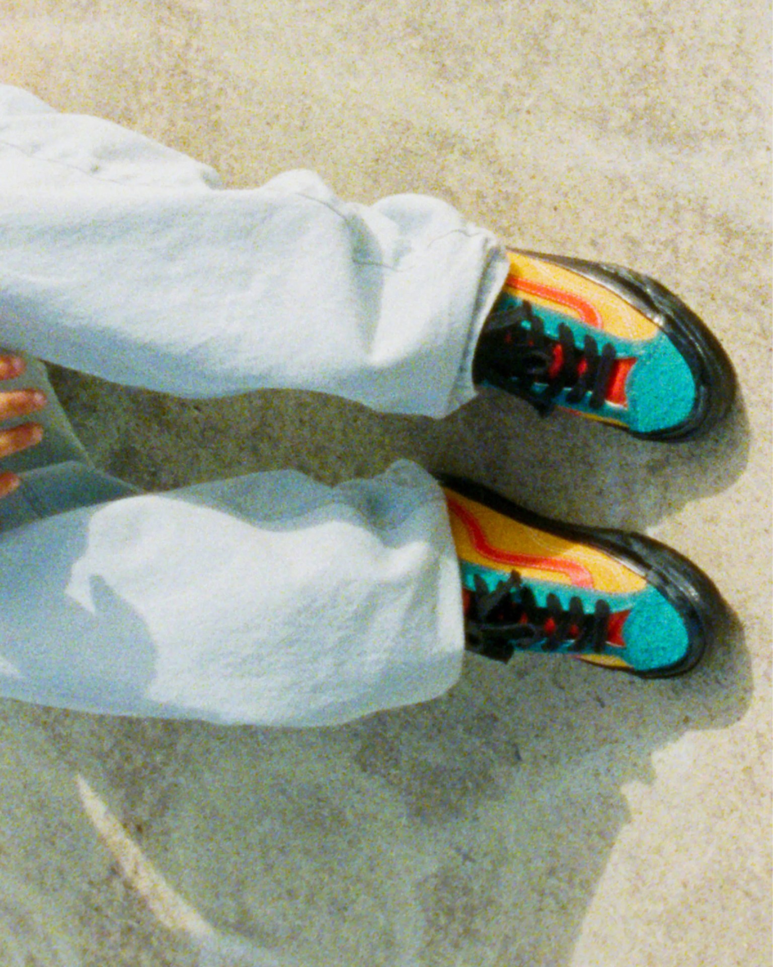 Person wearing light gray pants and colorful sneakers with teal, yellow, red, and black accents on a concrete floor.