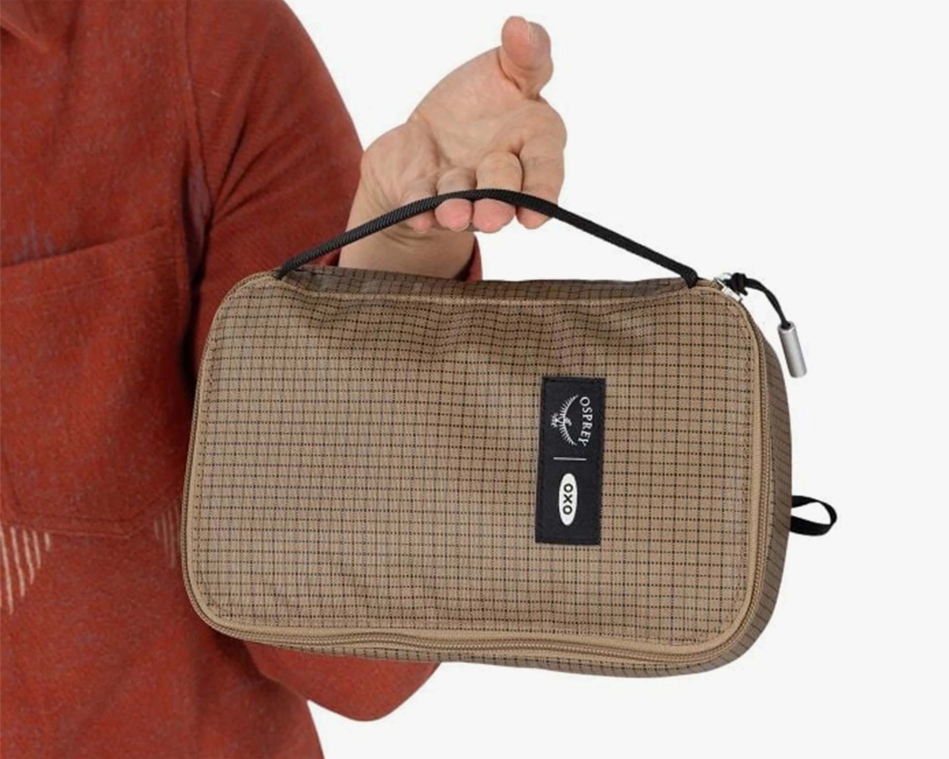 Beige checkered fabric pouch with black zipper and handle, held in a hand, featuring Osprey and OXO logos.