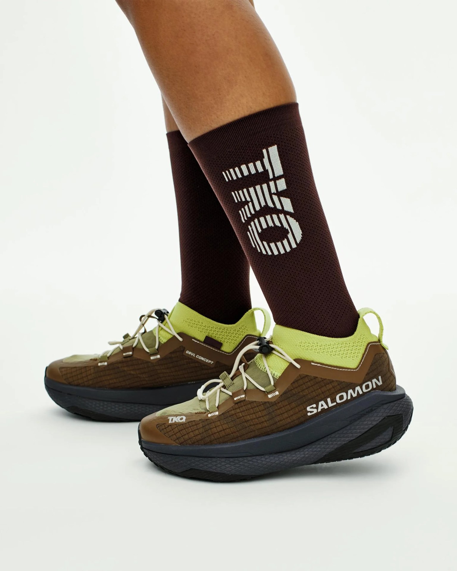 Brown and lime green Salomon TKO trail running shoes worn with dark brown socks featuring a white geometric logo.