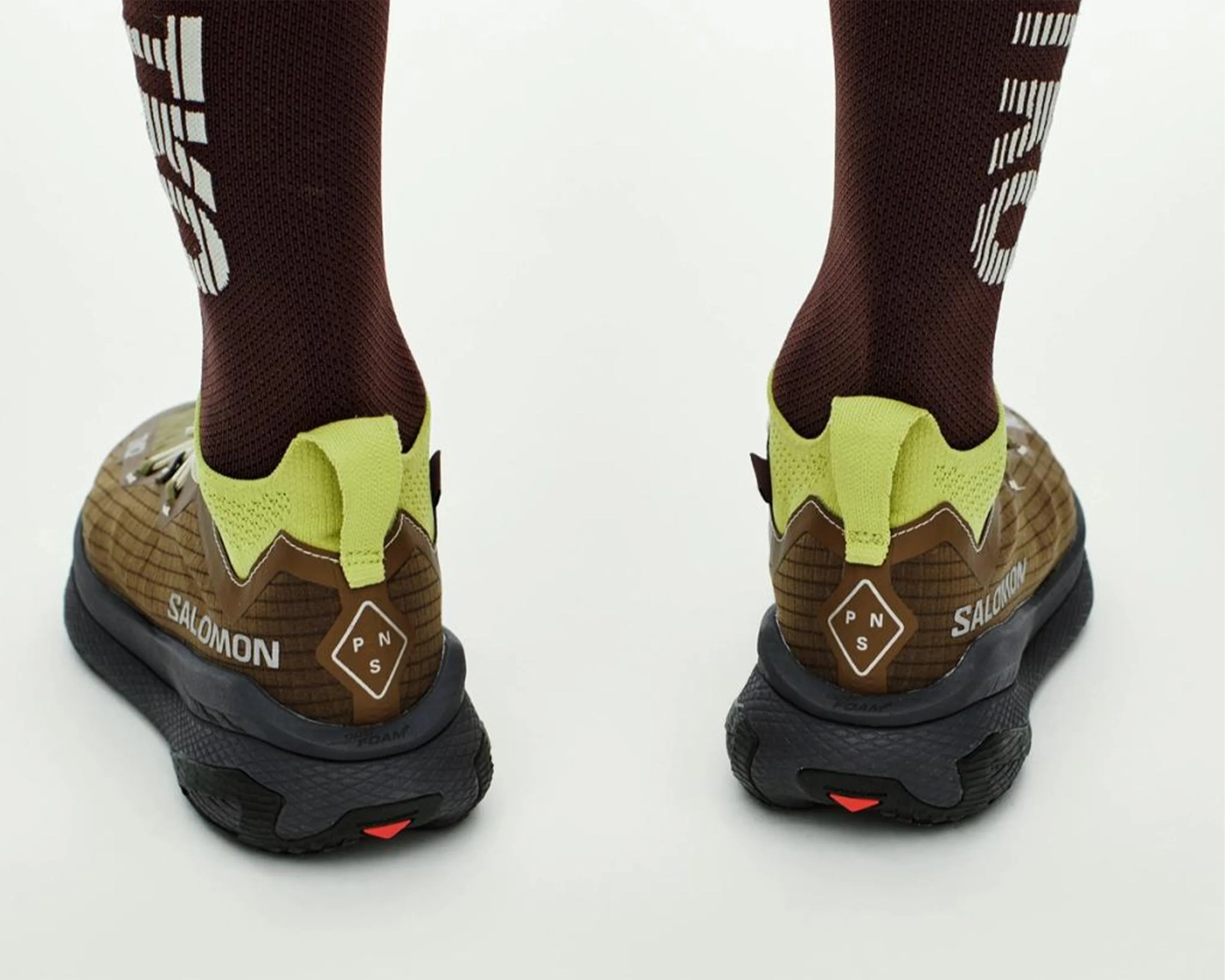 Brown Salomon trail running shoes with black soles and neon yellow heel tabs worn with brown socks.