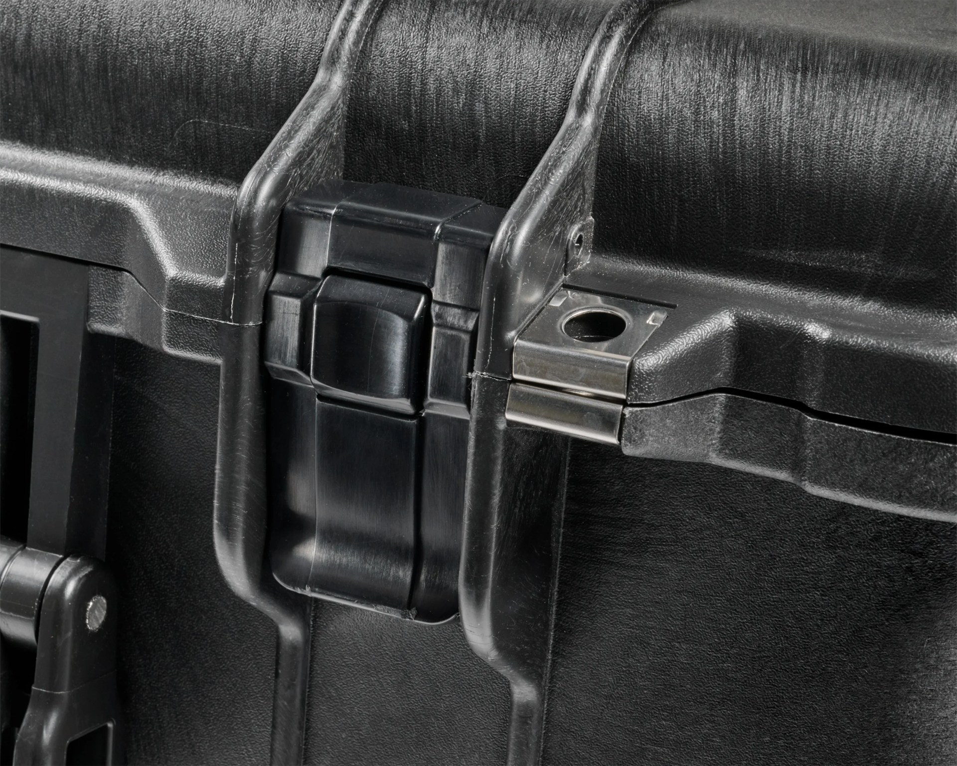 Close-up of a black plastic latch on a textured black hard case with metal hinge.