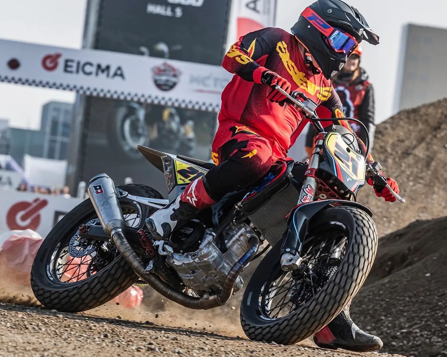 Motorcyclist in red and black gear riding a dirt bike with knobby tires on a dirt track.