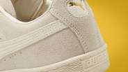 Close-up of beige suede Puma sneaker heel with gold Puma logo and textured sole against yellow background.