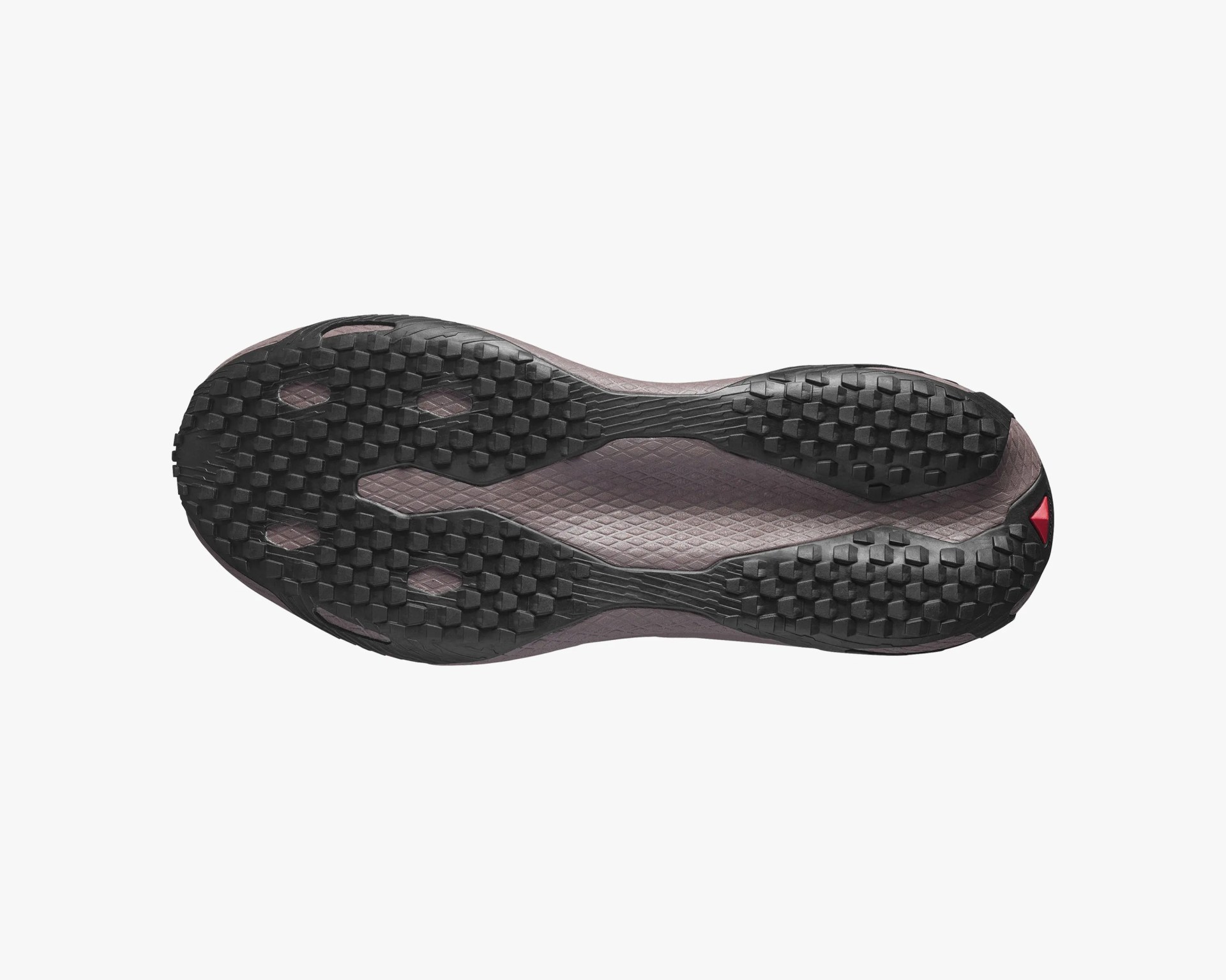 Black and dark purple textured rubber sole of a shoe with hexagonal tread pattern and a small red triangular detail.