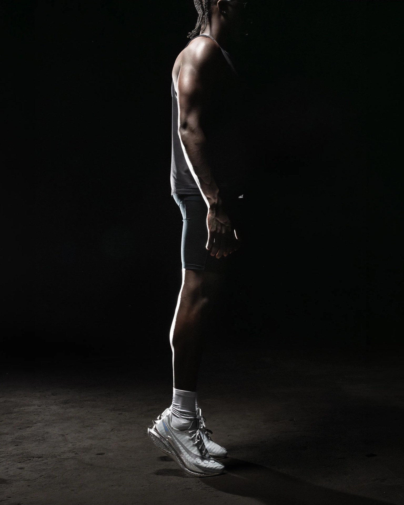 Person wearing white running shoes and black athletic shorts standing on a dark surface with a black background.