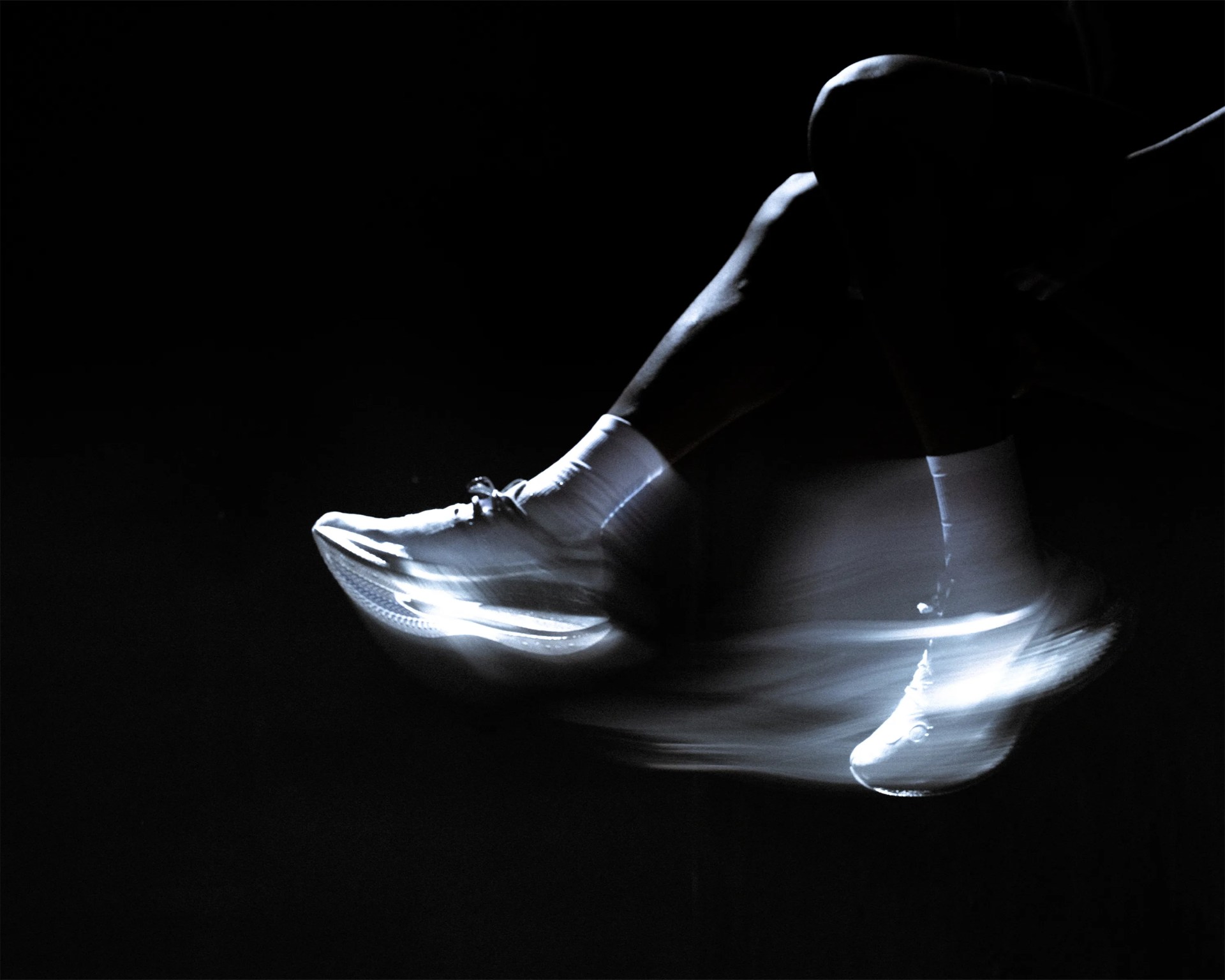 White athletic shoes with motion blur on a person's feet against a black background.
