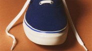 Navy blue canvas sneaker with white rubber sole and white laces on a brown surface.