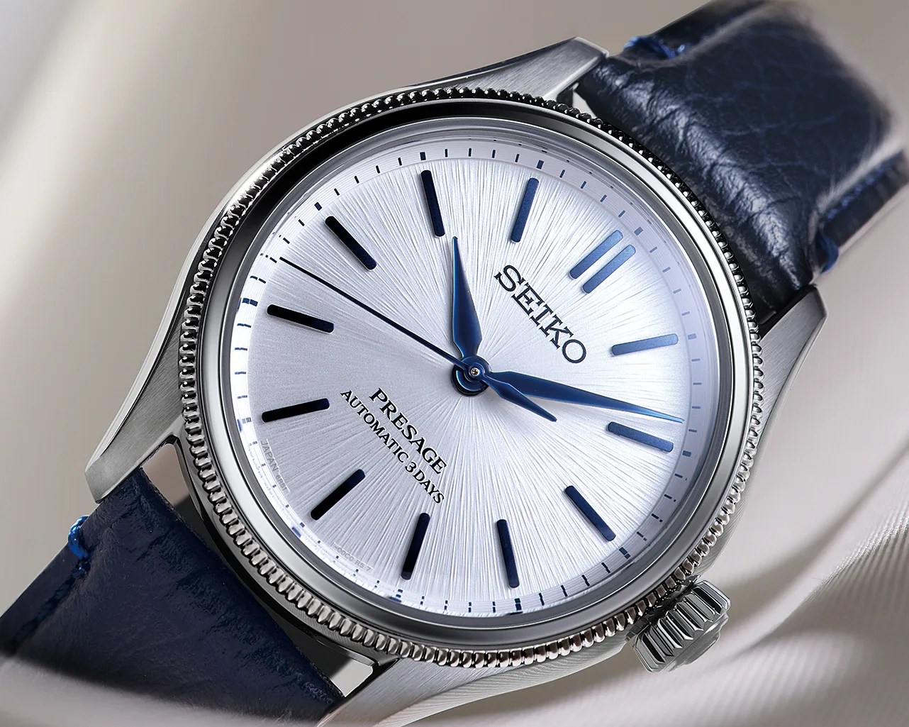 Silver Seiko Presage watch with blue hands and markers on a textured white dial and a dark blue leather strap.