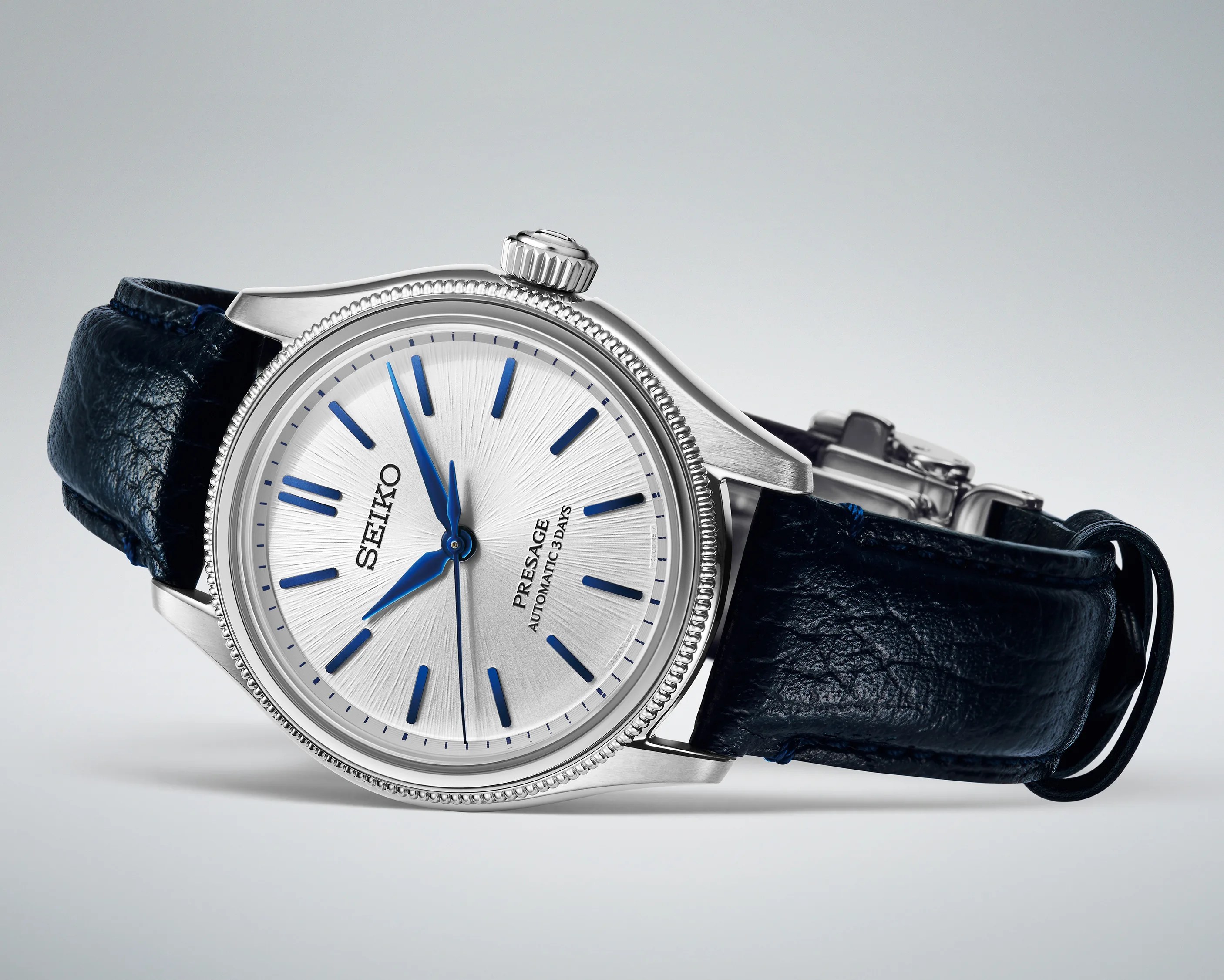 Silver Seiko Presage watch with blue hour markers and hands on a black leather strap.
