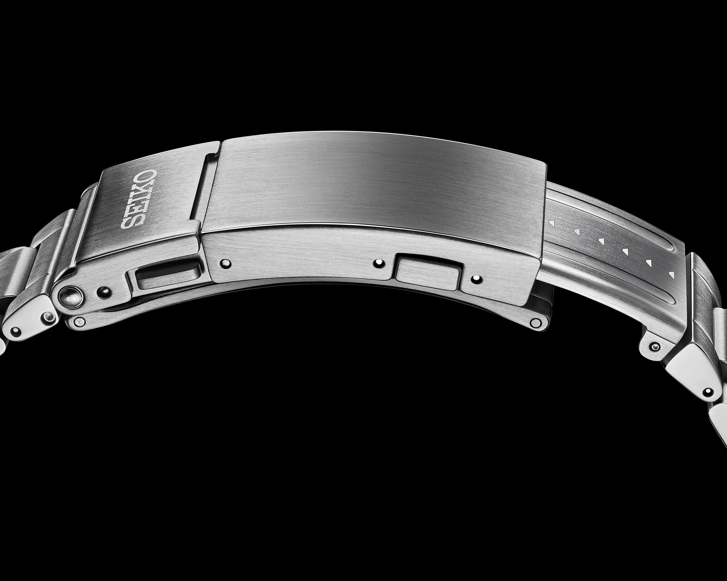 Brushed stainless steel Seiko watch clasp with push-button release on a black background.