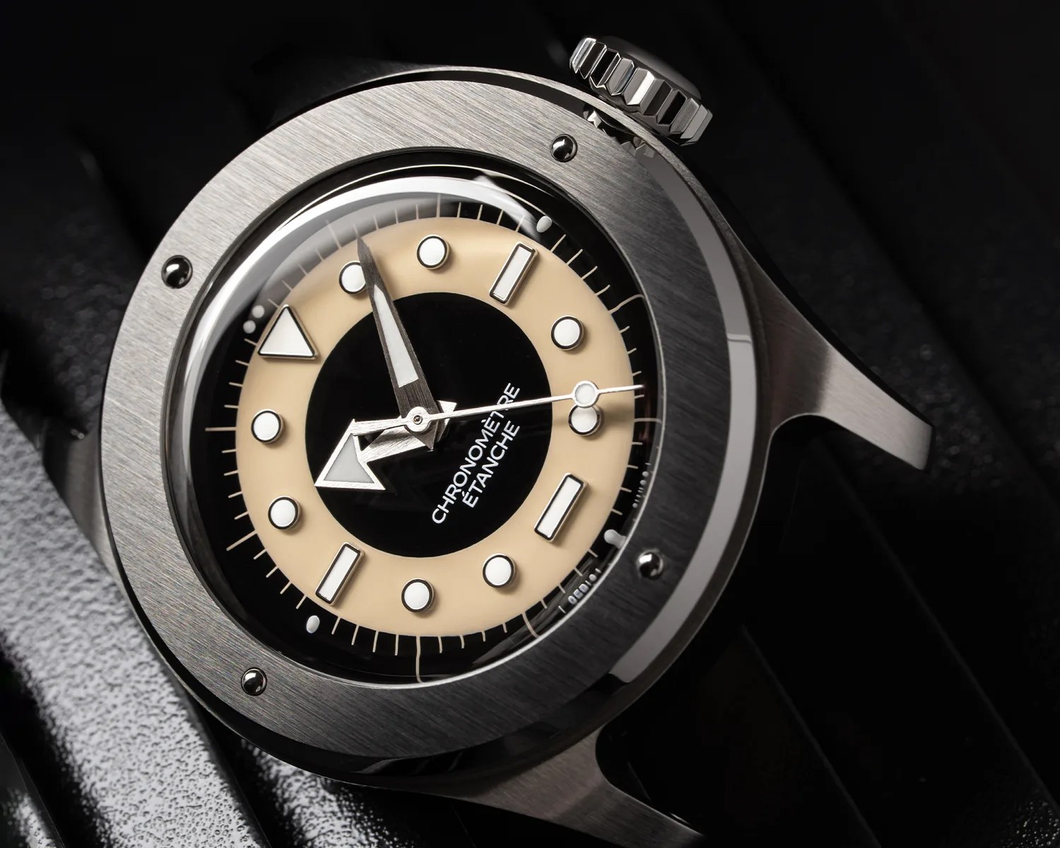 Close-up of a stainless steel wristwatch with a beige and black dial, large arrow hour hand, and "CHRONOM&Egrave;TRE &Eacute;TANCHE" text.