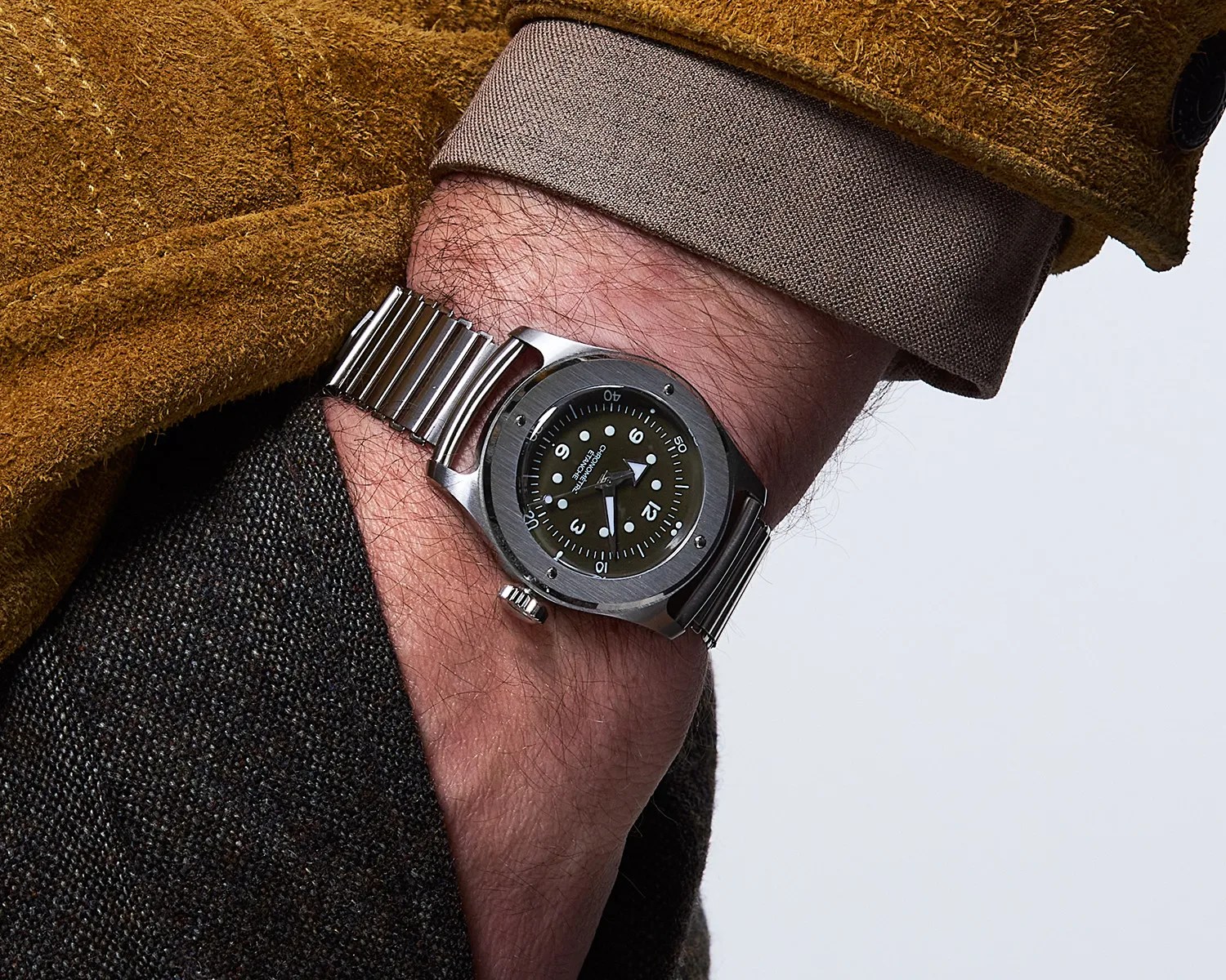 Stainless steel wristwatch with black dial and silver metal bracelet worn on a wrist with brown and gray clothing.