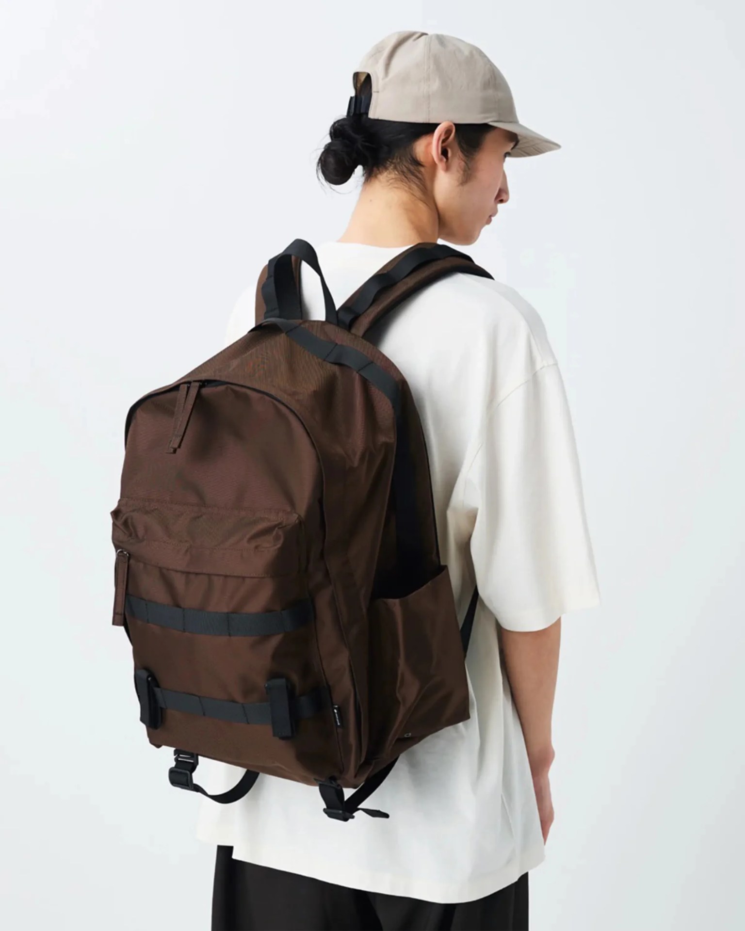 Brown backpack with black straps worn by a person in a white shirt and beige cap.