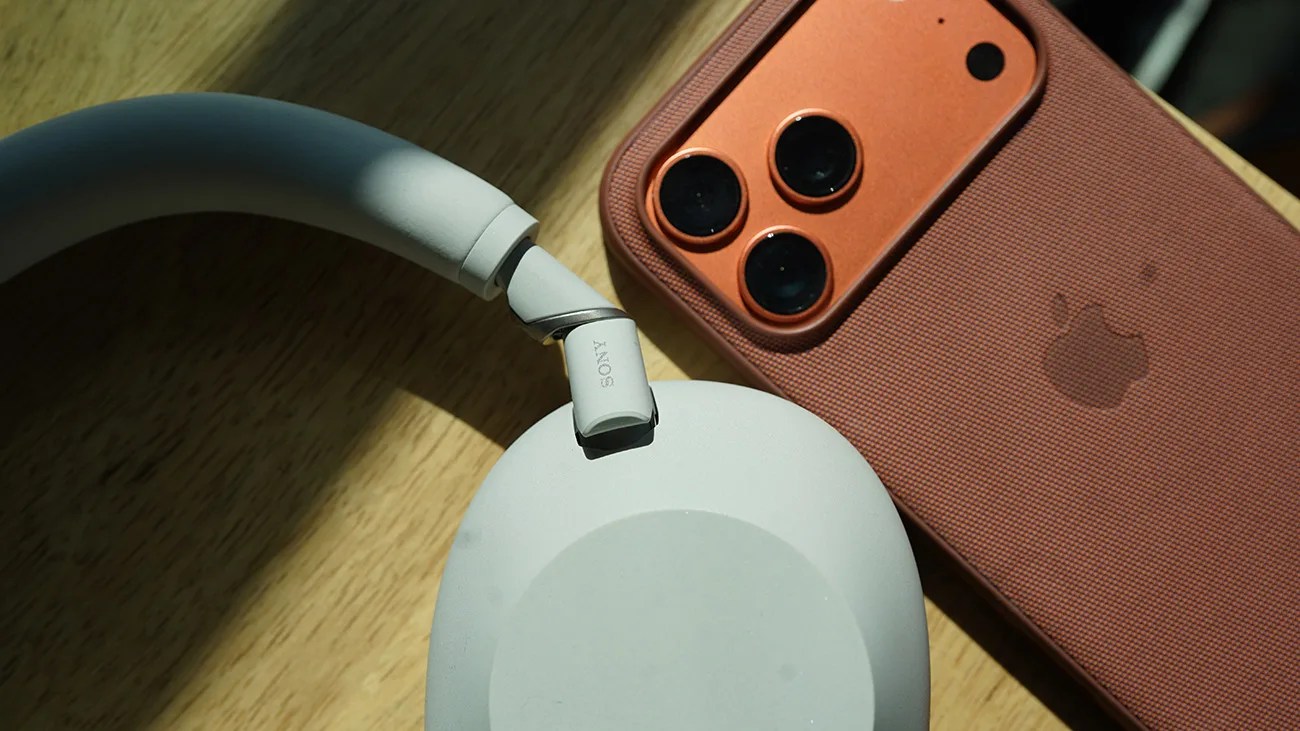 White Sony over-ear headphones next to an orange iPhone with a textured case on a wooden surface.