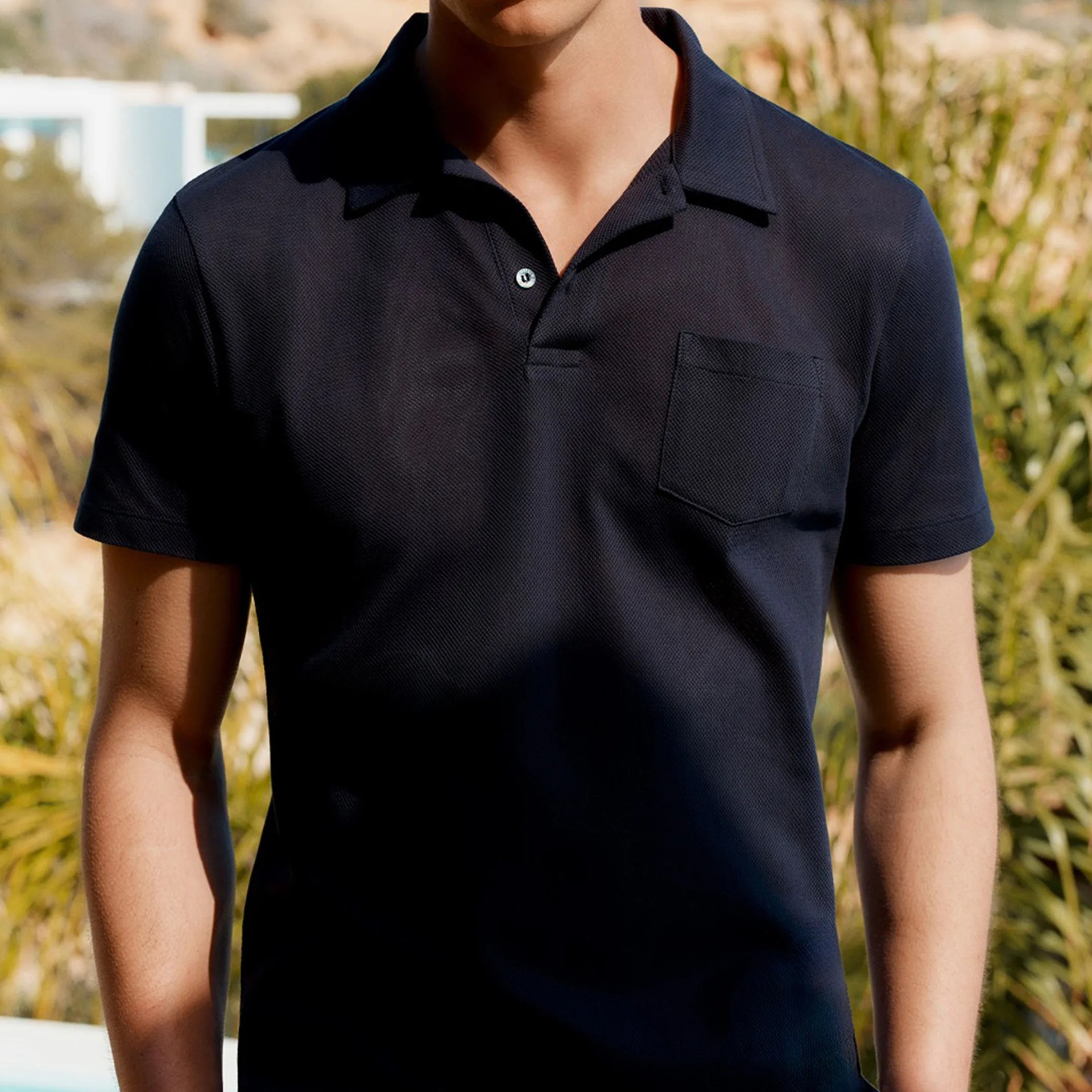 Navy blue textured short-sleeve polo shirt with a chest pocket and one button fastened.