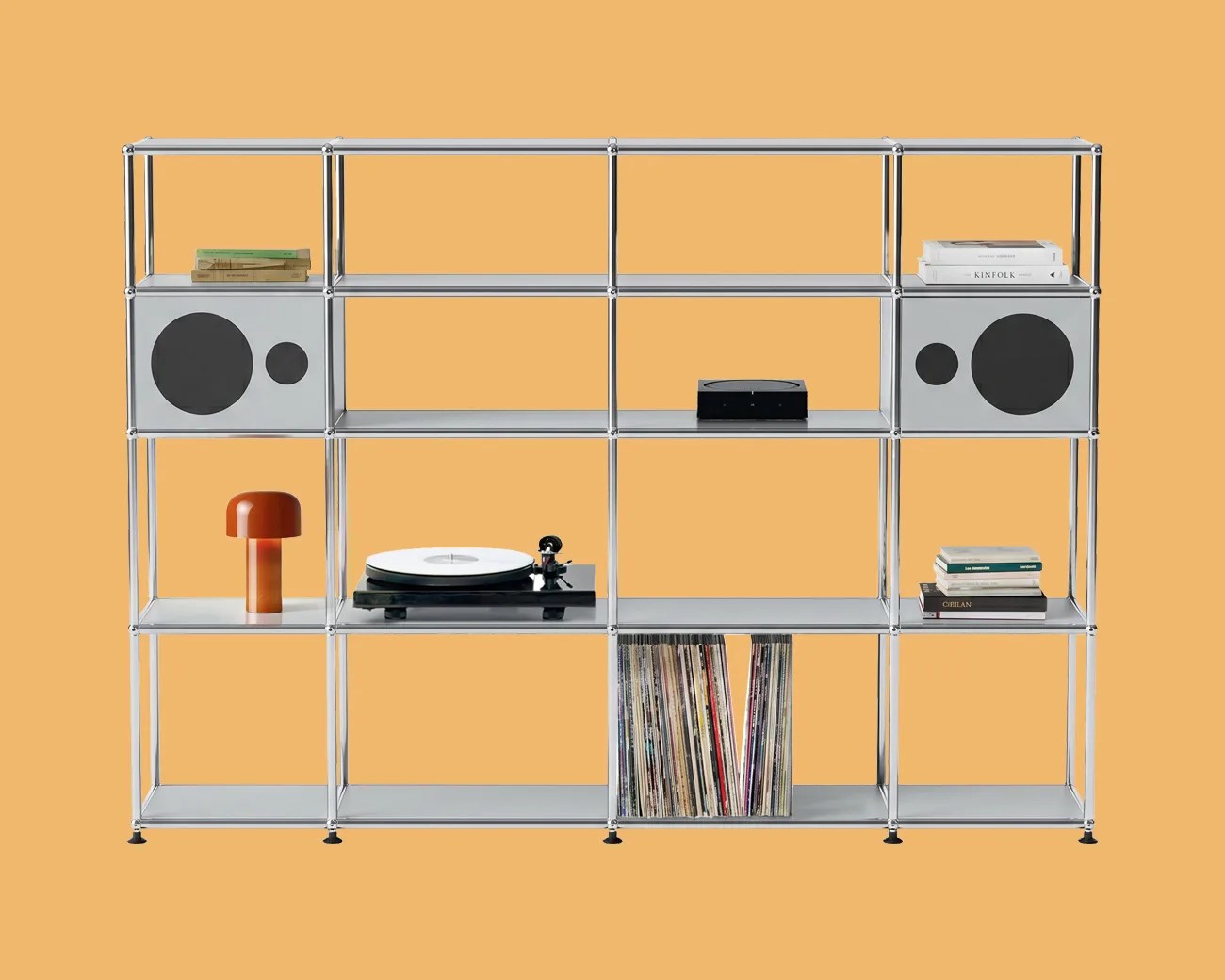 White metal shelving unit with built-in speakers, a record player, vinyl records, books, and an orange table lamp against a mustard background.