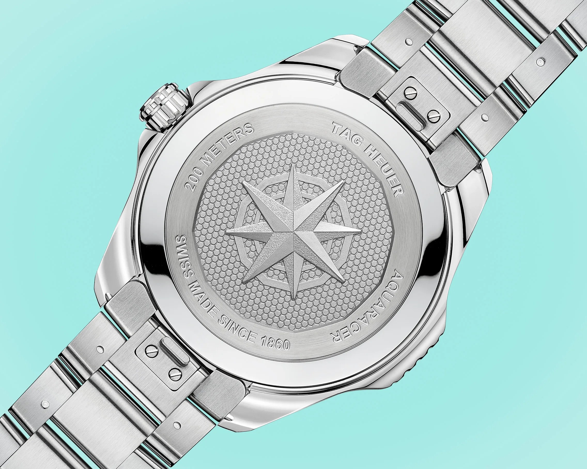 Back of a silver TAG Heuer Aquaracer watch with engraved compass rose and metal bracelet on a turquoise background.