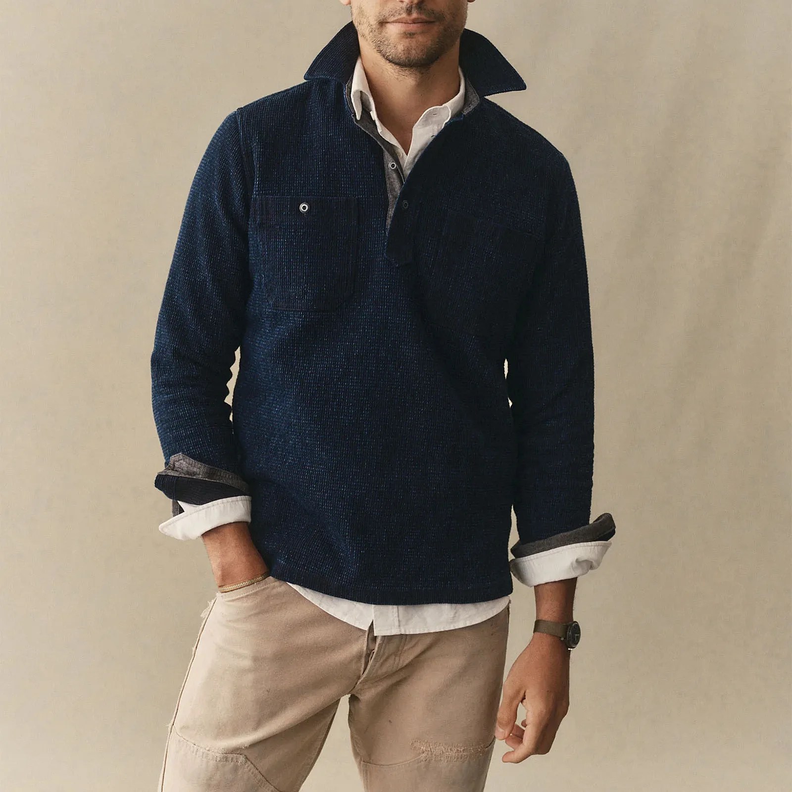 Navy textured pullover with chest pockets worn over a white button-up shirt and beige pants.