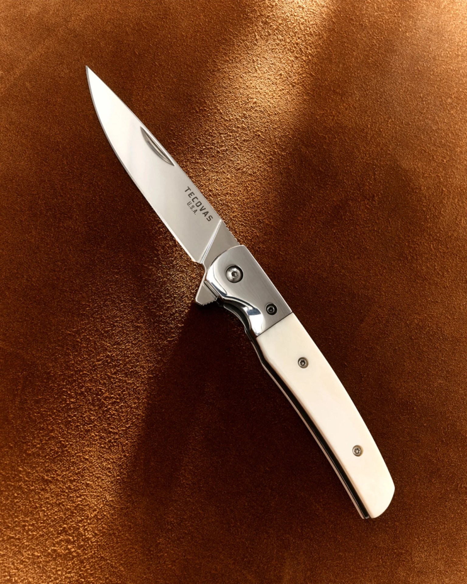Folding knife with a polished silver blade and white handle on a brown textured surface.