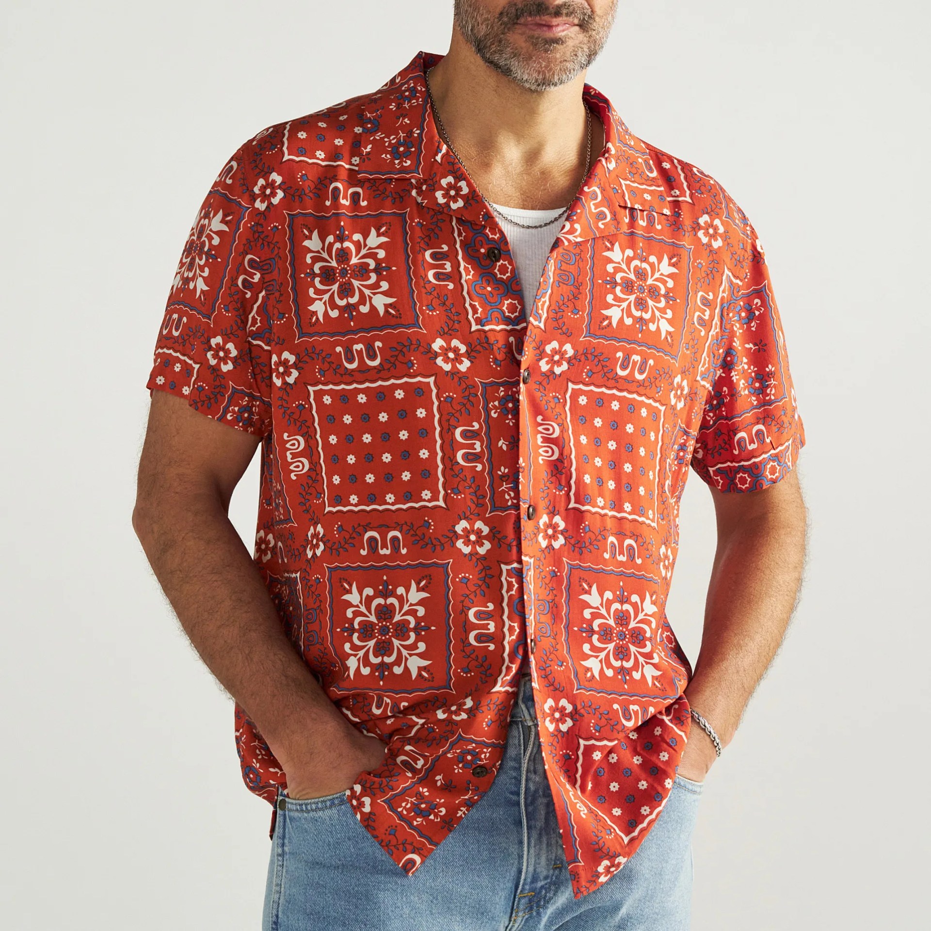 Rust-orange short-sleeve button-up shirt with white and blue floral and geometric patterns worn over a white tank top.