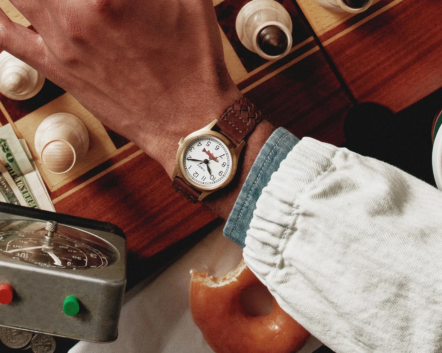 Wrist with a Timex watch featuring a white dial and brown leather strap over a chessboard with white chess pieces.