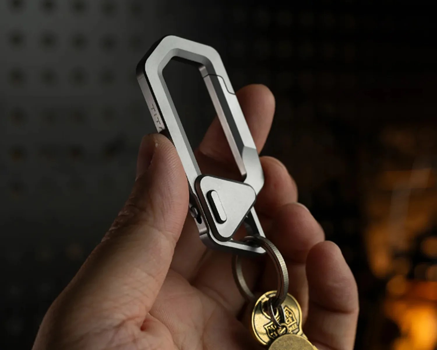 Hand holding a silver metal carabiner keychain with attached keys against a dark background.
