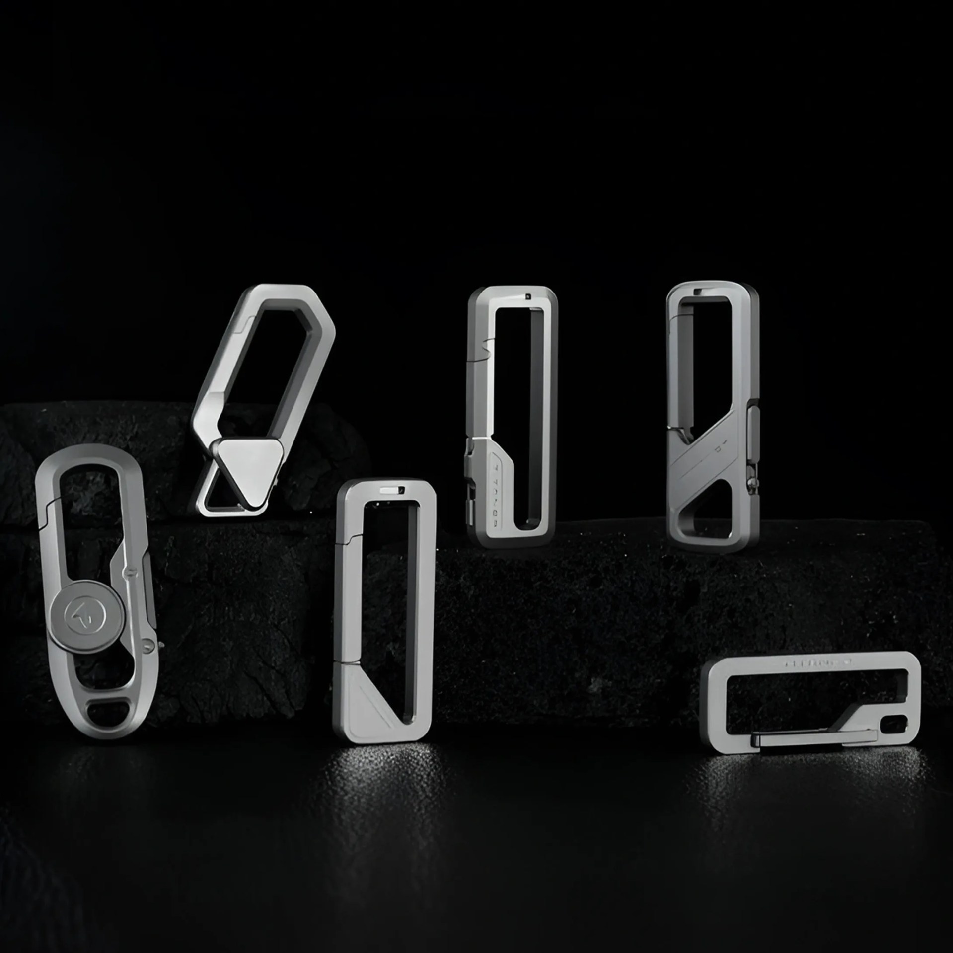 Set of silver-gray rectangular and polygonal carabiner clips with various locking mechanisms on a black textured surface.