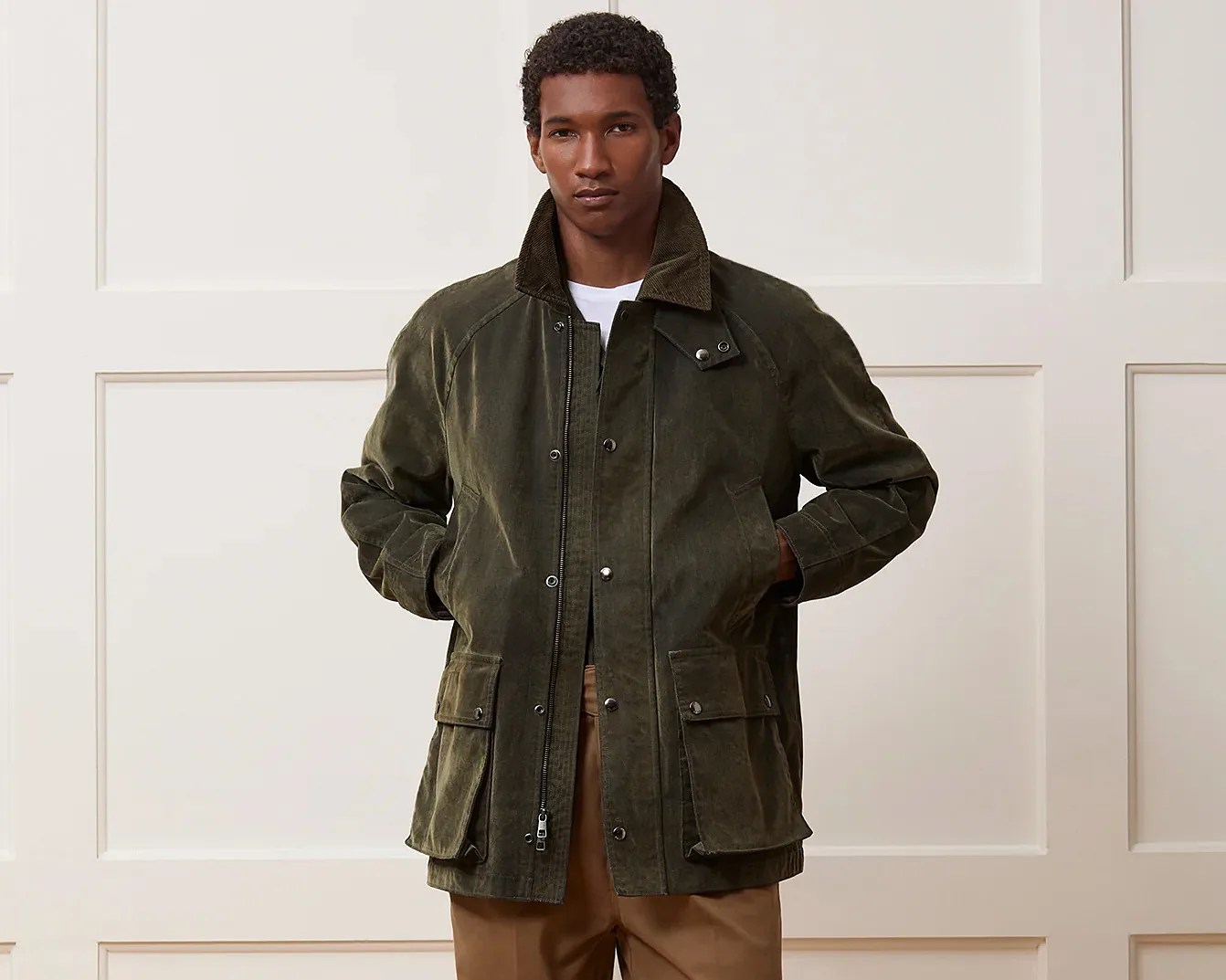 Olive green waxed cotton jacket with corduroy collar and flap pockets worn by a person.