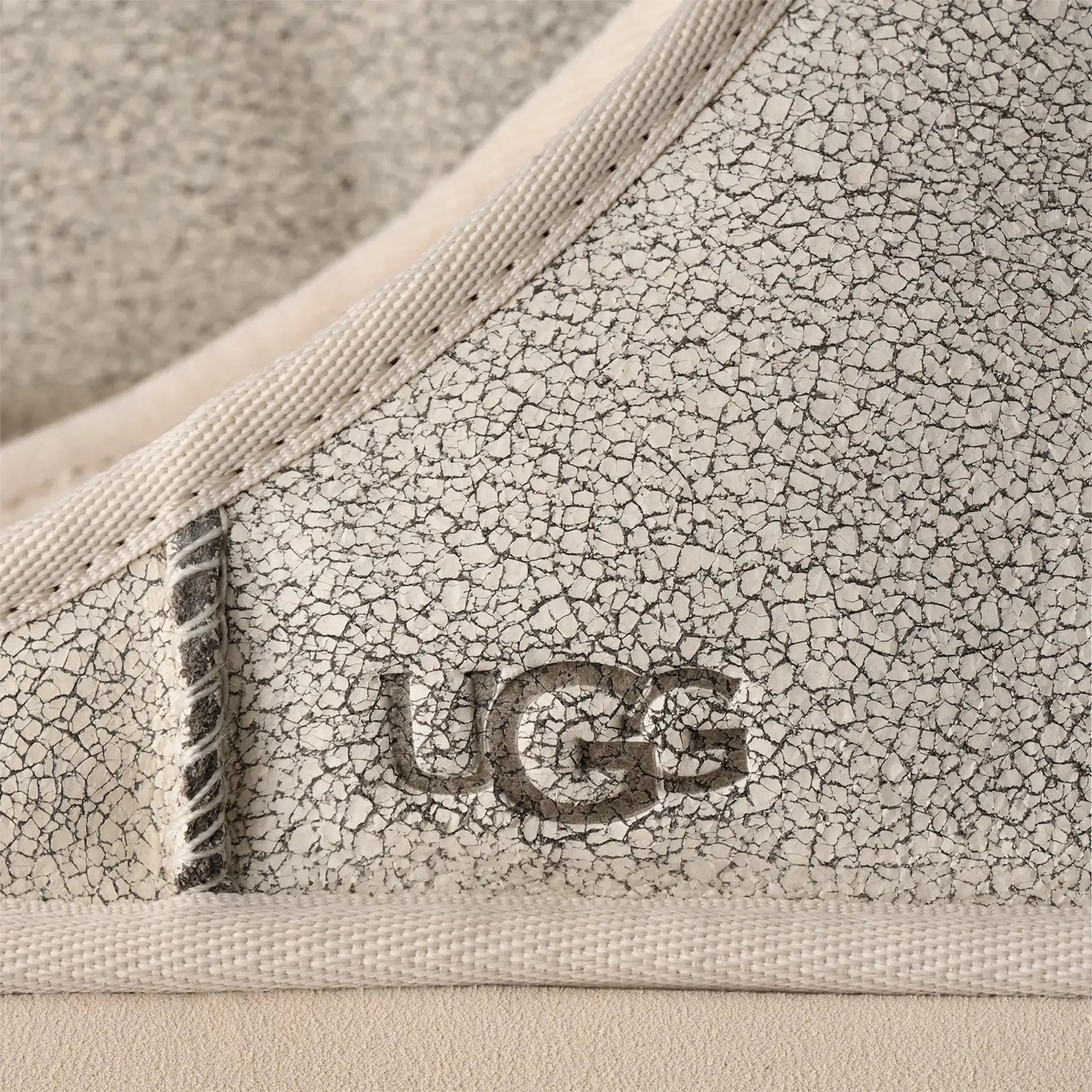 Close-up of cracked beige leather with UGG logo embossed and beige fabric trim.
