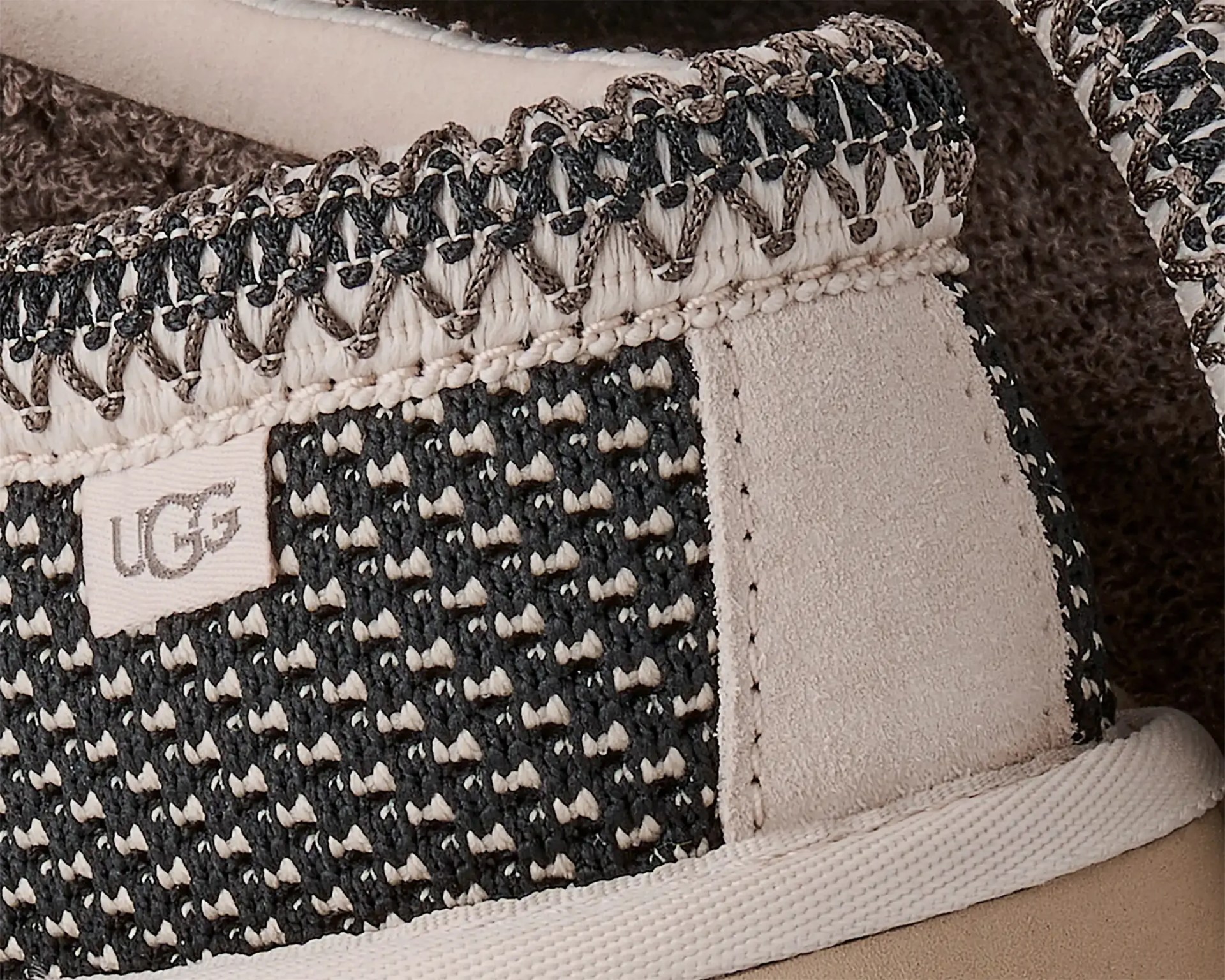 Close-up of a black and beige woven UGG shoe with detailed stitching and suede accents.