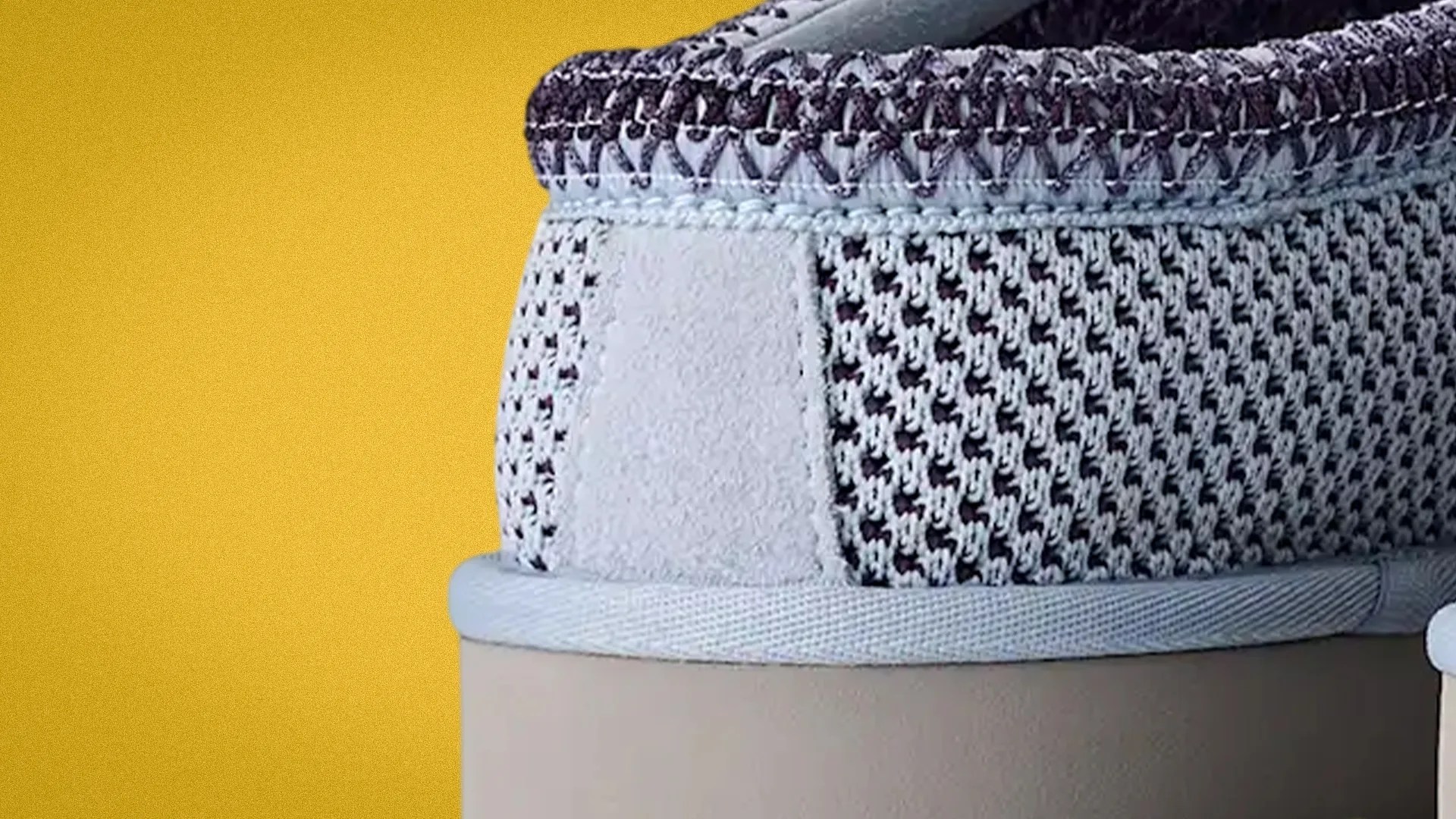 Close-up of the heel area of a knit sneaker with a suede patch and a beige sole against a yellow background.