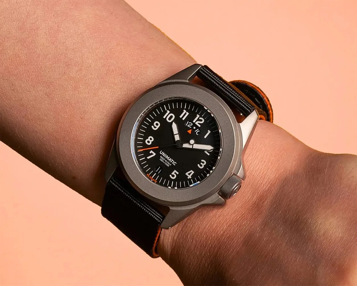 Wristwatch with a black dial, white numerals, and a black strap with orange edges worn on a wrist.