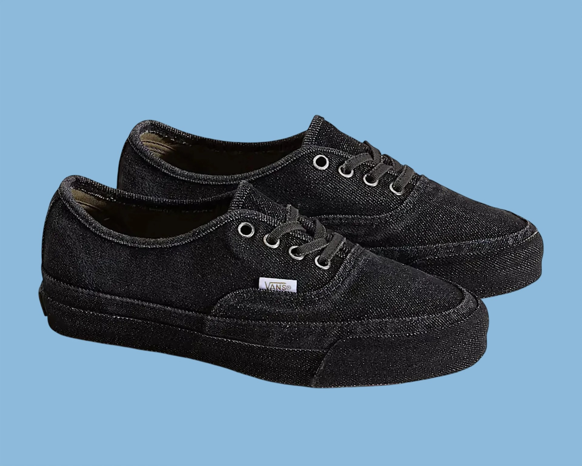 Pair of black Vans canvas sneakers with black laces on a blue background.
