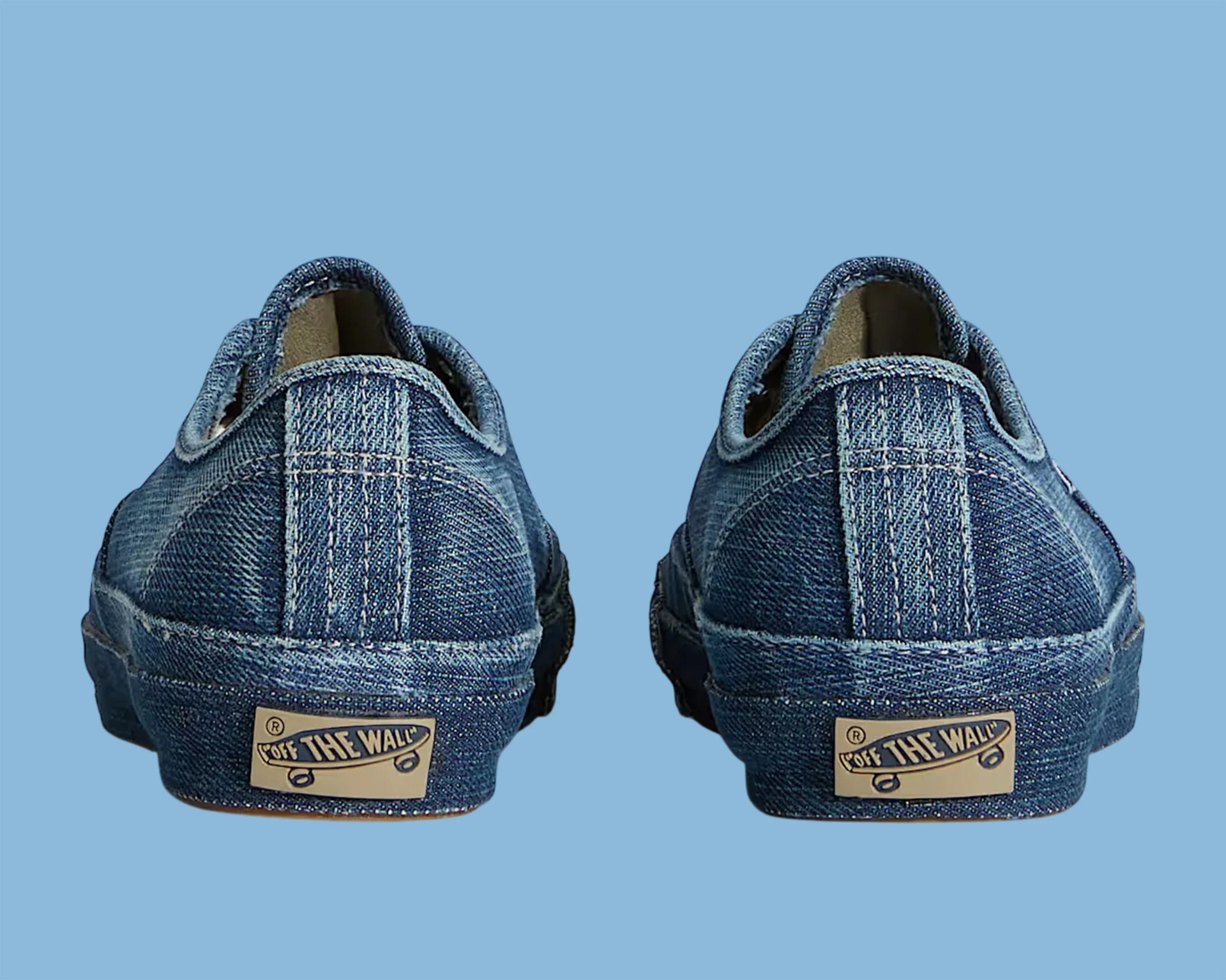 Pair of blue denim Vans sneakers viewed from the back on a light blue background.