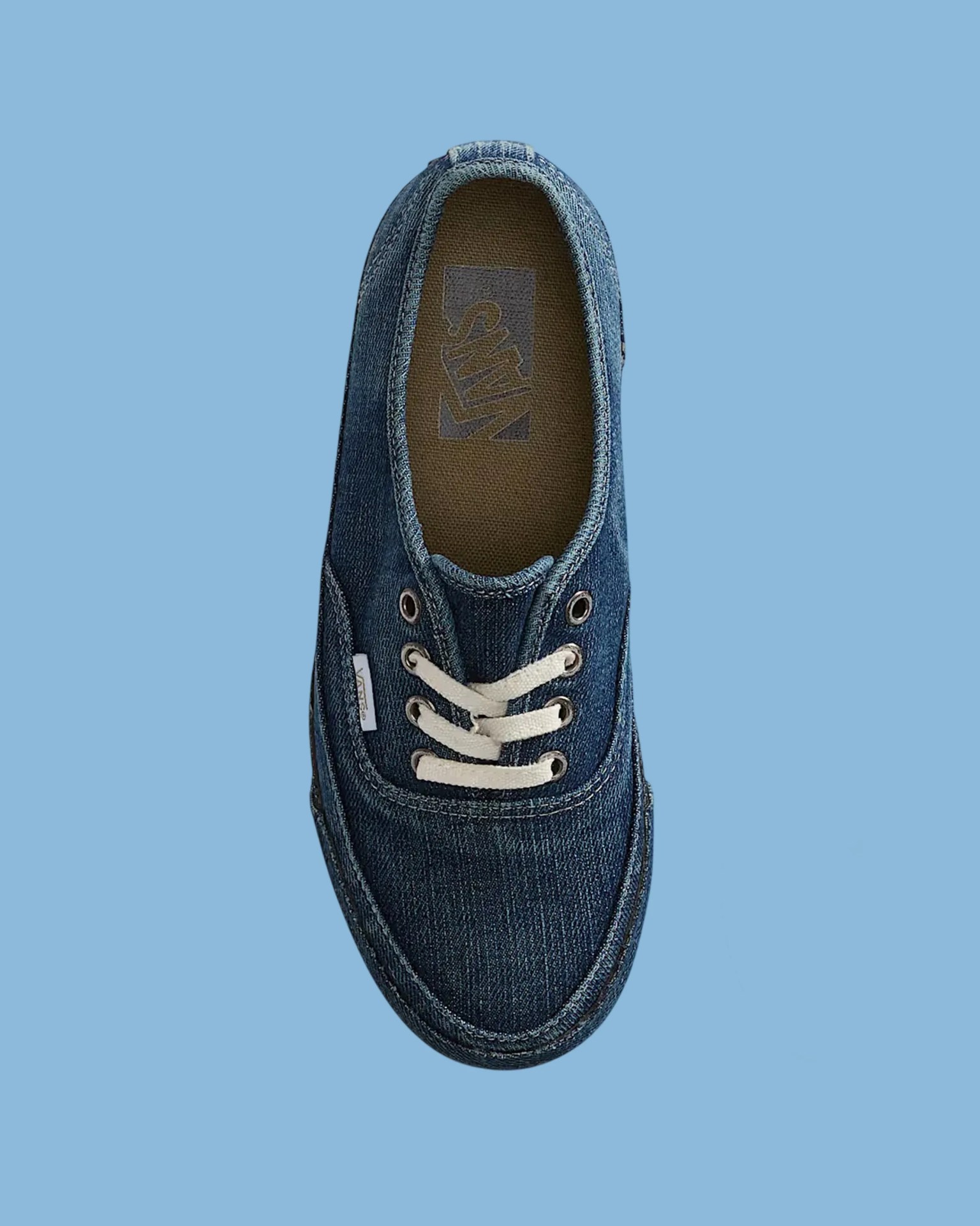 Top view of a blue denim Vans sneaker with white laces on a light blue background.