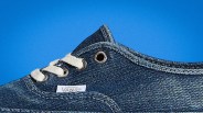 Close-up of a blue denim Vans sneaker with white laces and metal eyelets against a blue background.