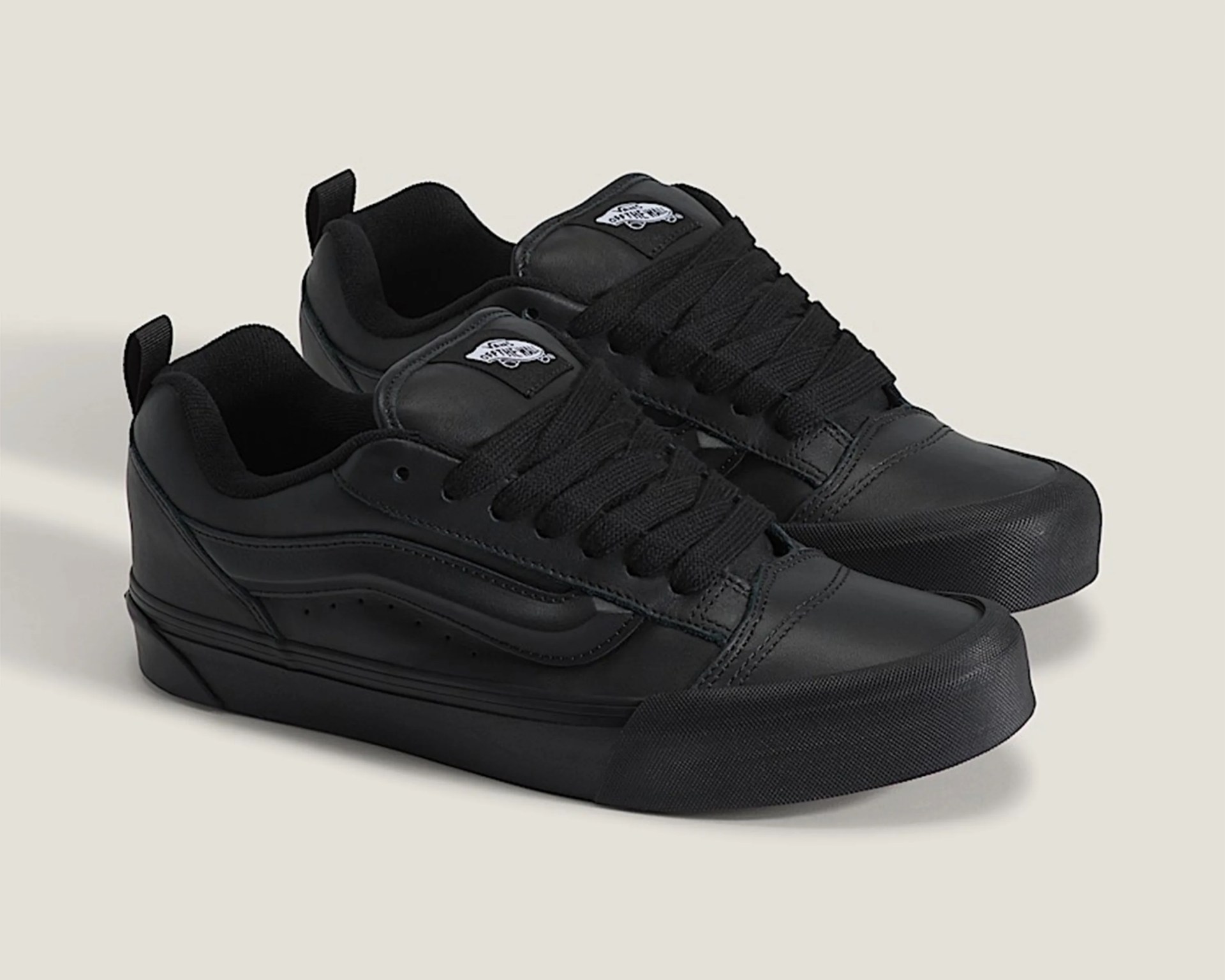 Pair of black Vans leather sneakers with thick black laces and rubber soles on a light background.