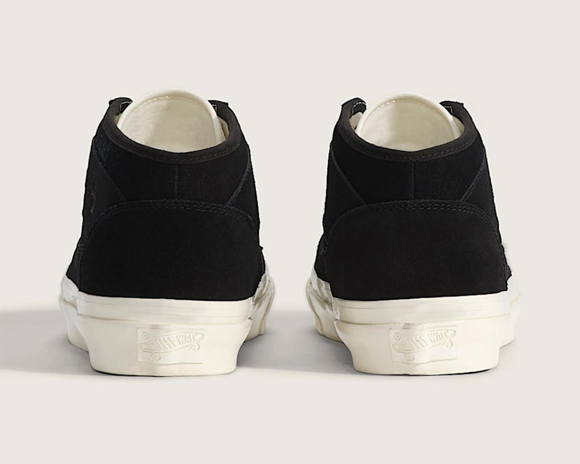 Pair of black suede Vans sneakers viewed from the back with white rubber soles.