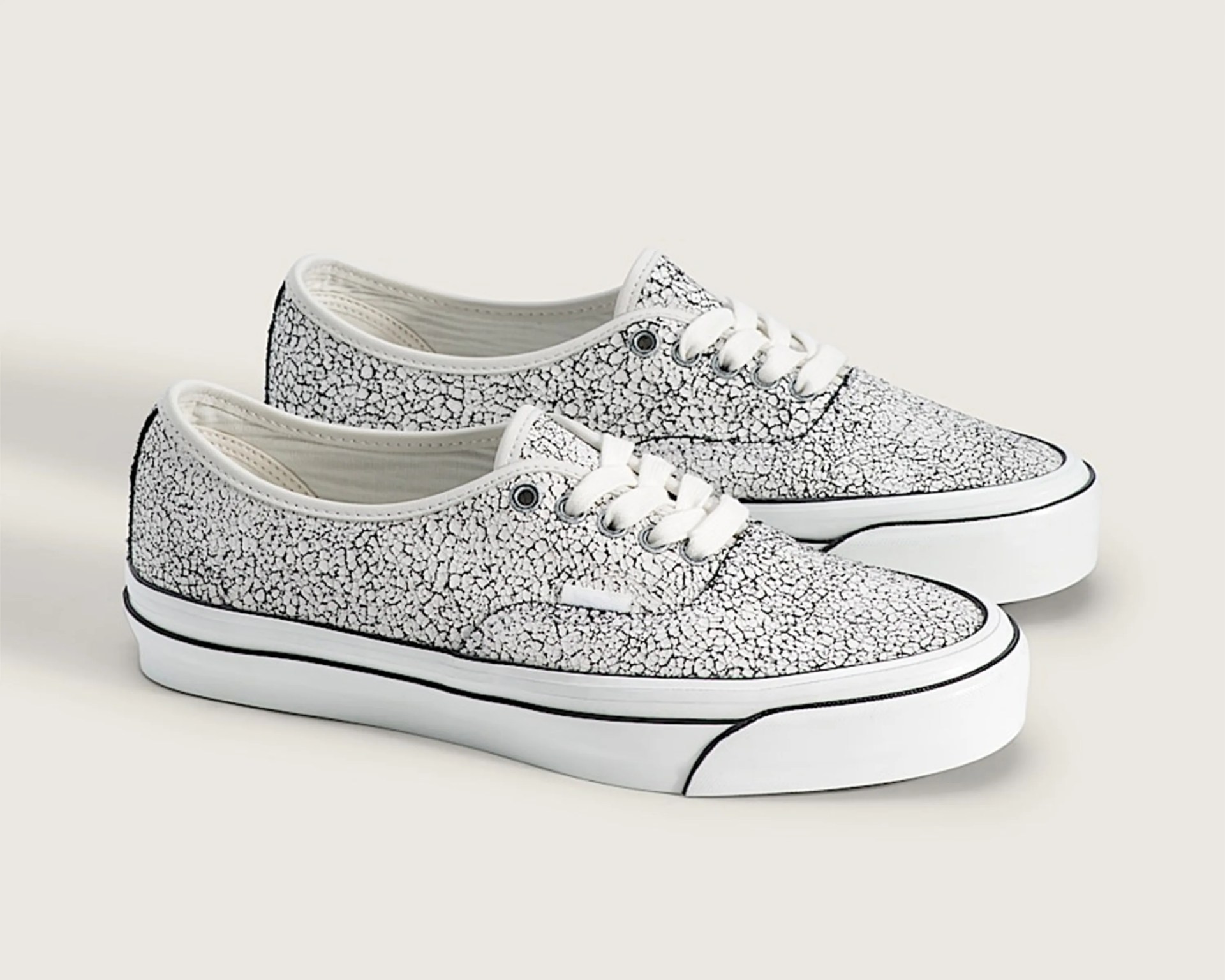 Pair of white low-top sneakers with black crackle pattern and white laces on a light background.