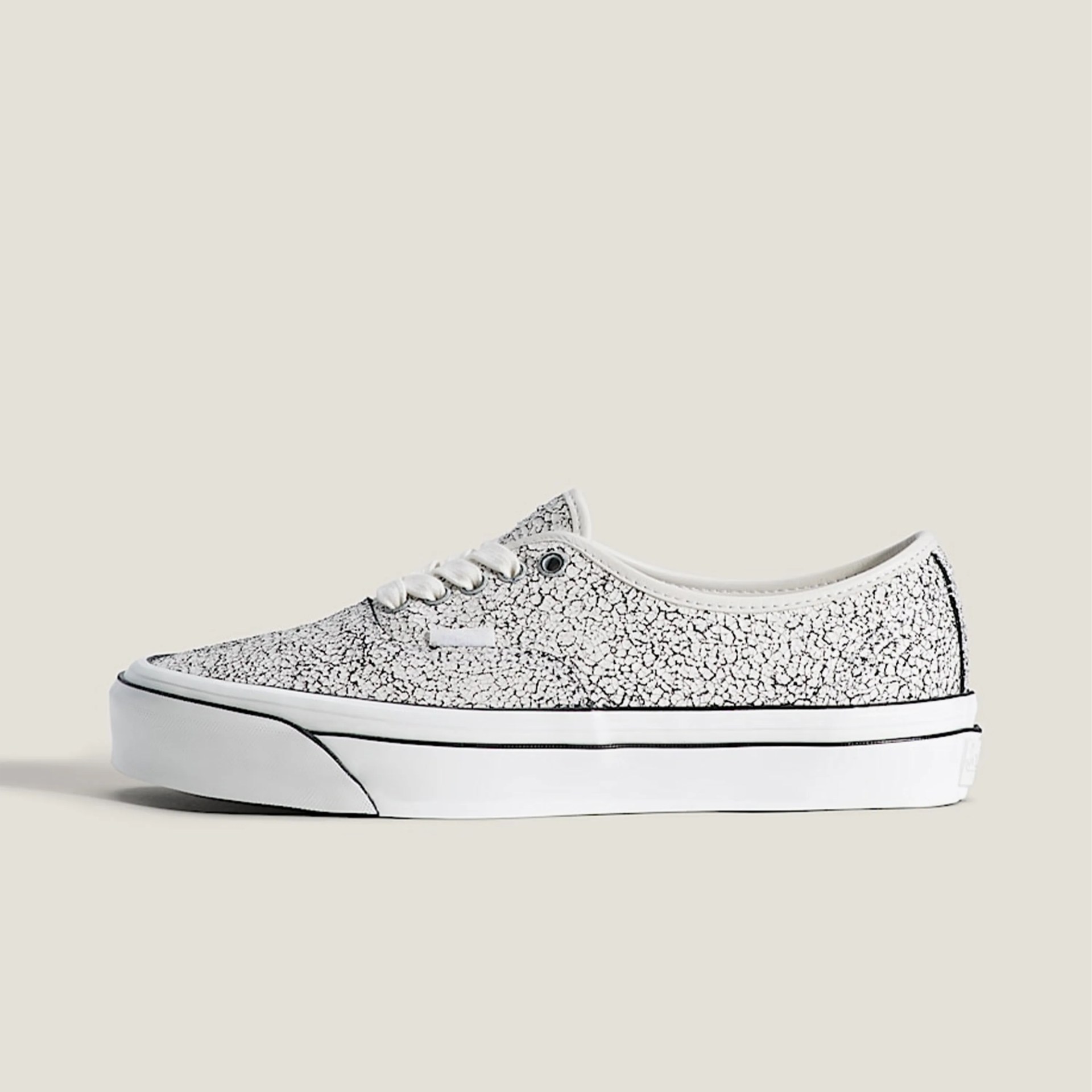 White low-top sneaker with black cracked pattern and thick white sole with black stripe on beige background.