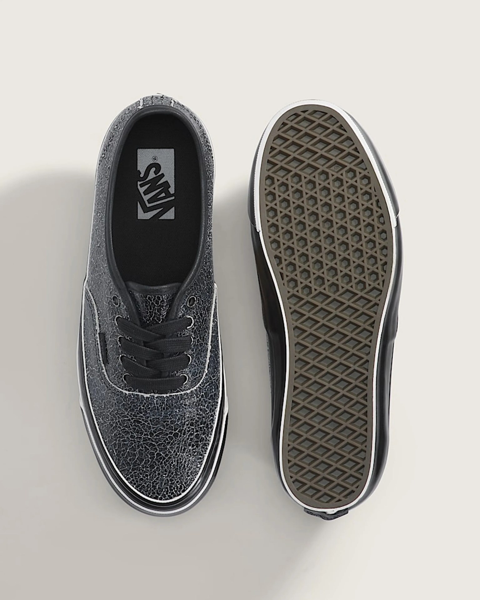 Pair of black Vans sneakers with cracked texture, one showing top view and the other showing waffle-pattern sole.