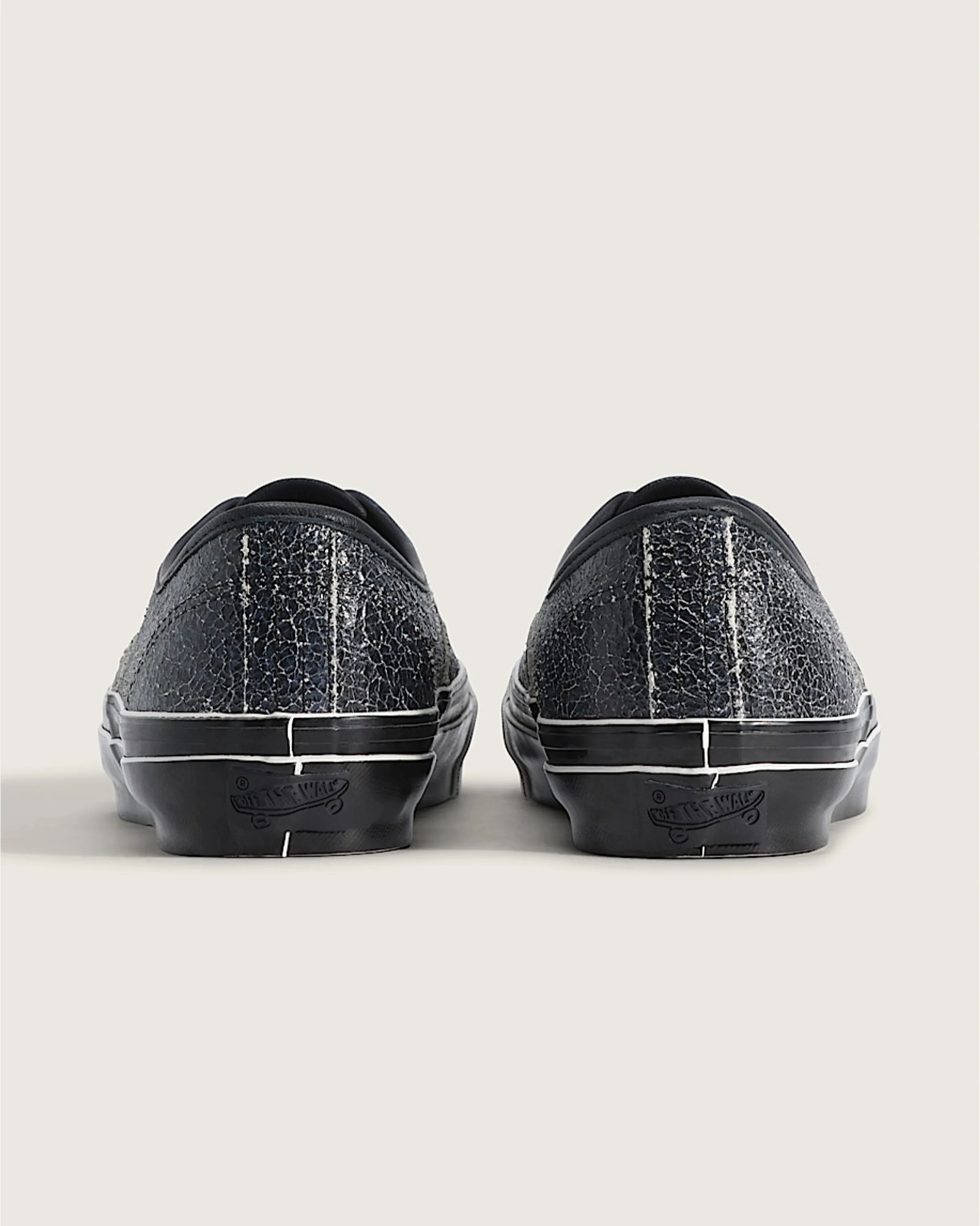 Pair of black Vans sneakers with cracked leather texture shown from the back on a light background.