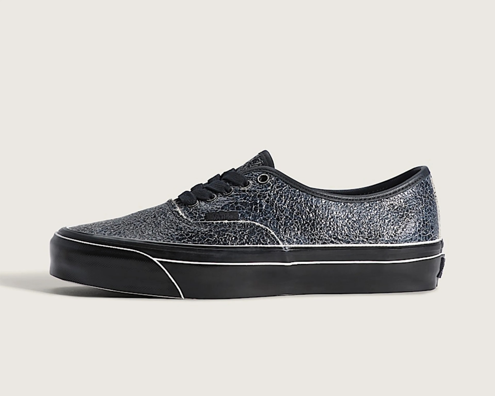Black Vans sneaker with cracked leather texture and black rubber sole with white trim.