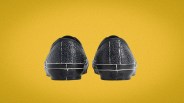 Pair of black cracked leather Vans sneakers shown from the back on a yellow background.